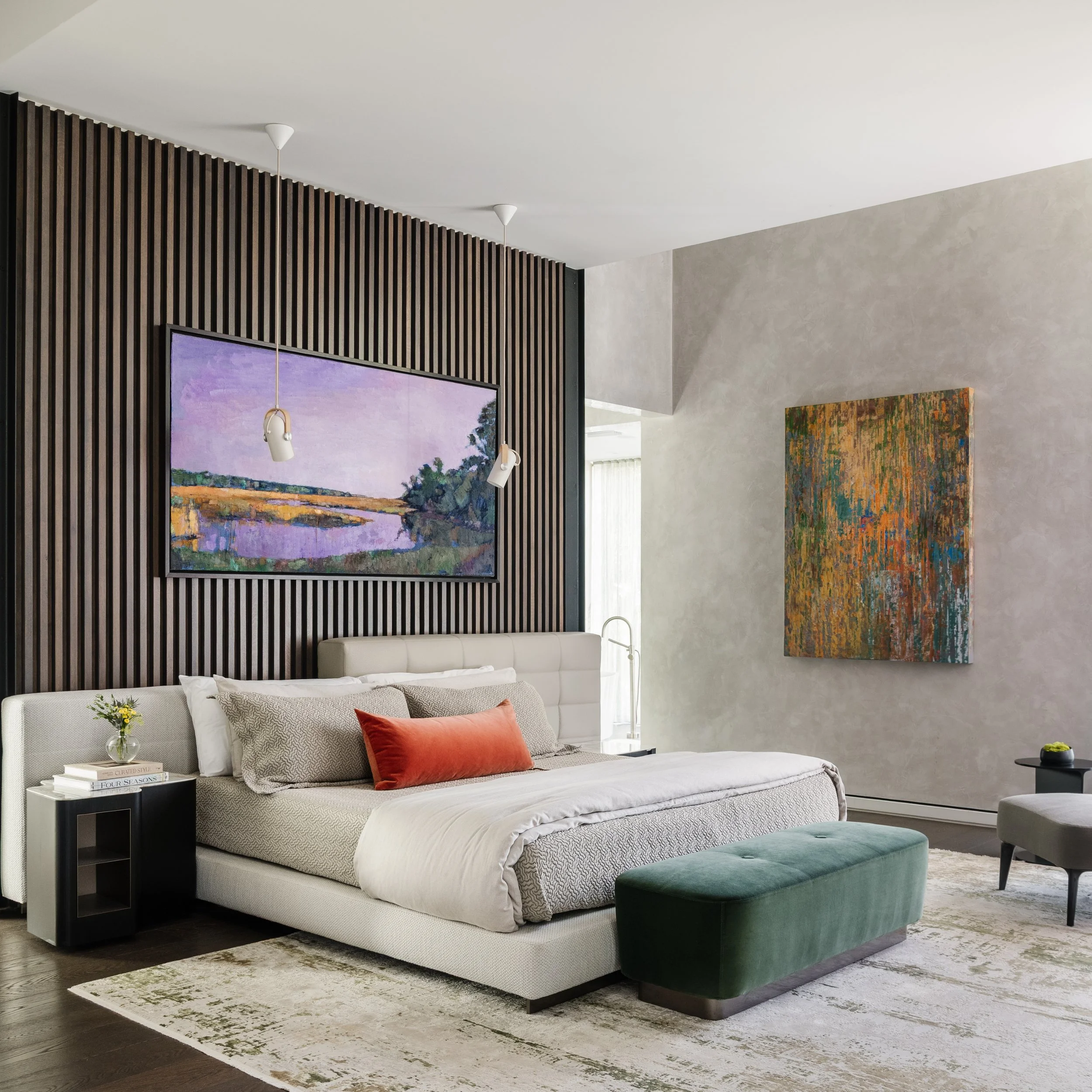 Modern living room with white sofa, orange and patterned pillows, green ottoman, abstract wall art, black bookshelf, and a floor lamp.