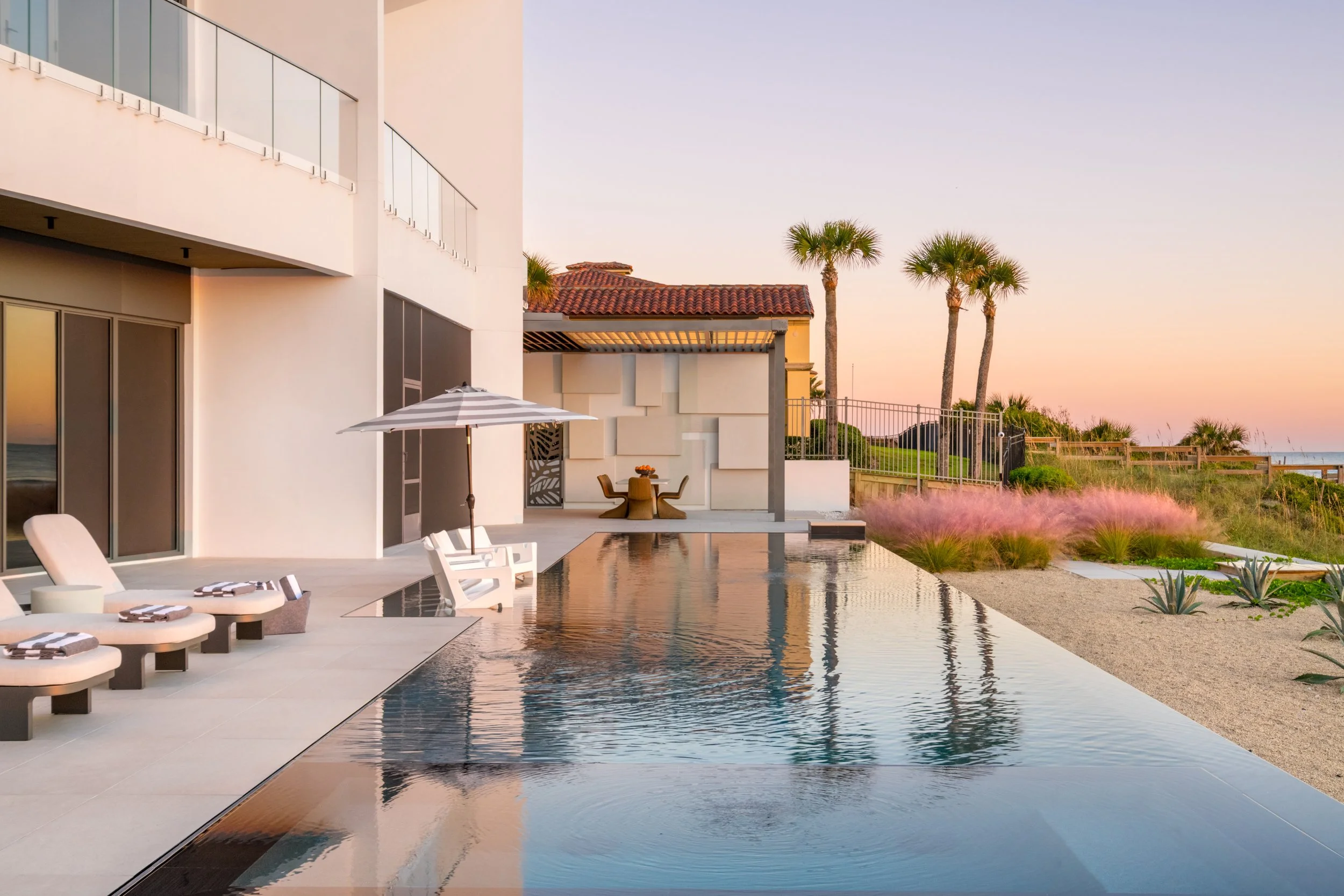 Modern house with outdoor pool, palm trees, and patio furniture at sunset.