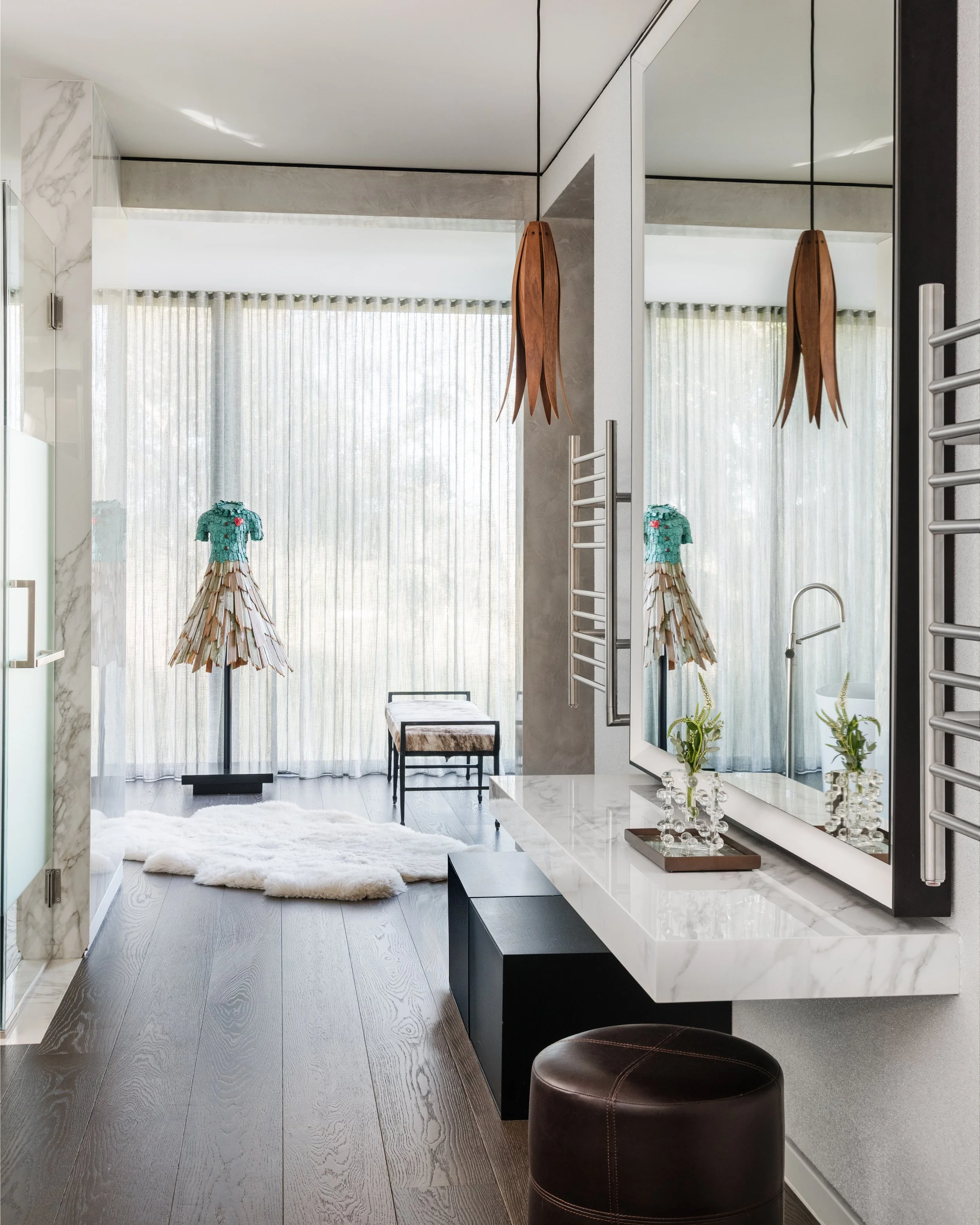 Modern interior living space with large mirror, curtains, two wooden umbrella-shaped hanging light fixtures, small seating bench, white plush rug, wooden flooring, and decorative vases with plants.