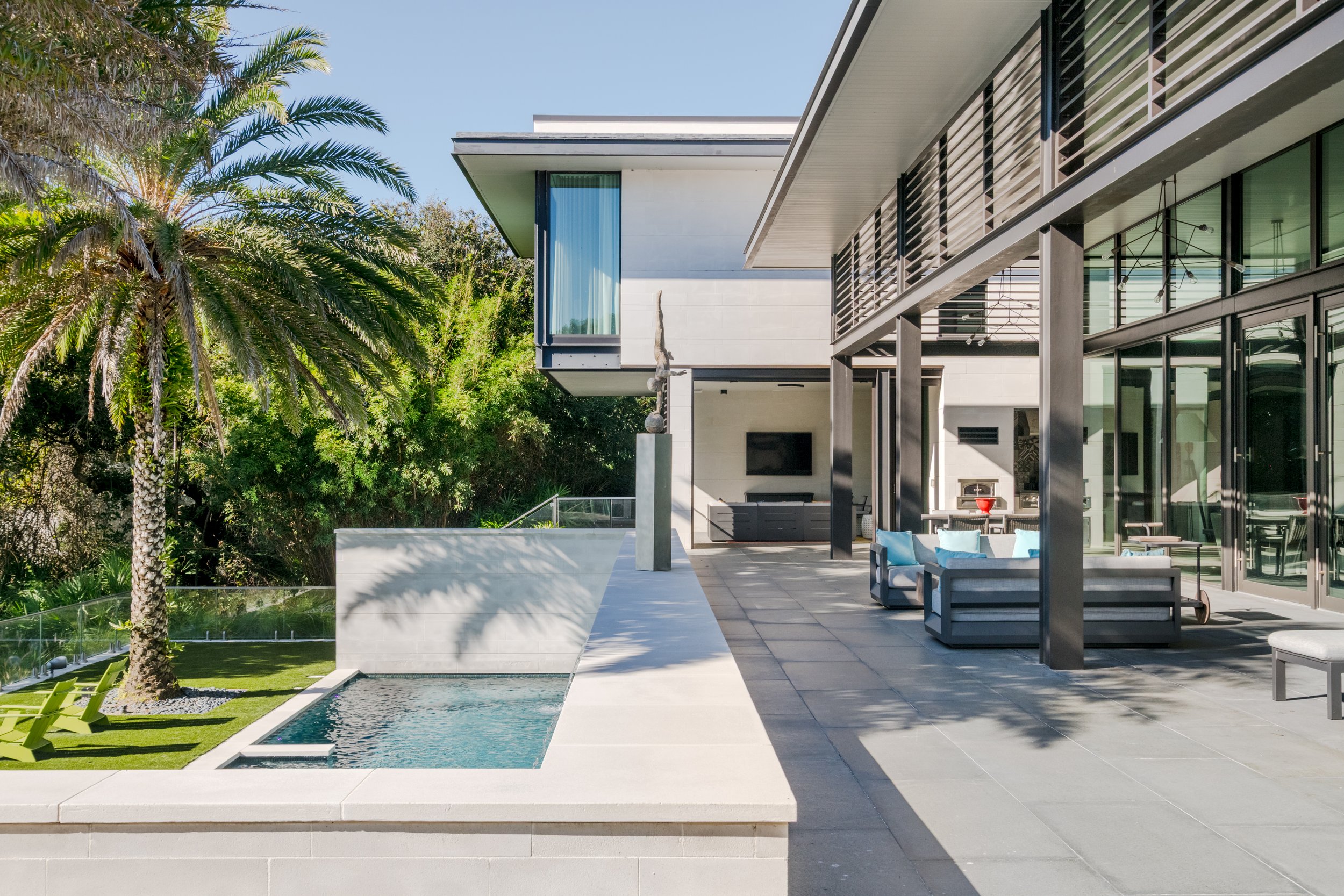 Modern house exterior with a swimming pool, patio furniture, and lush greenery.