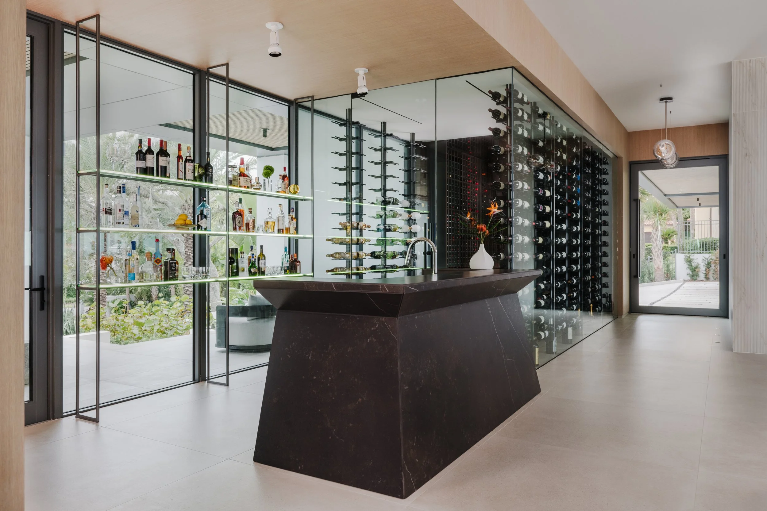 Modern home's wine cellar and bar area with glass walls, wine racks, and a black marble island with a sink.