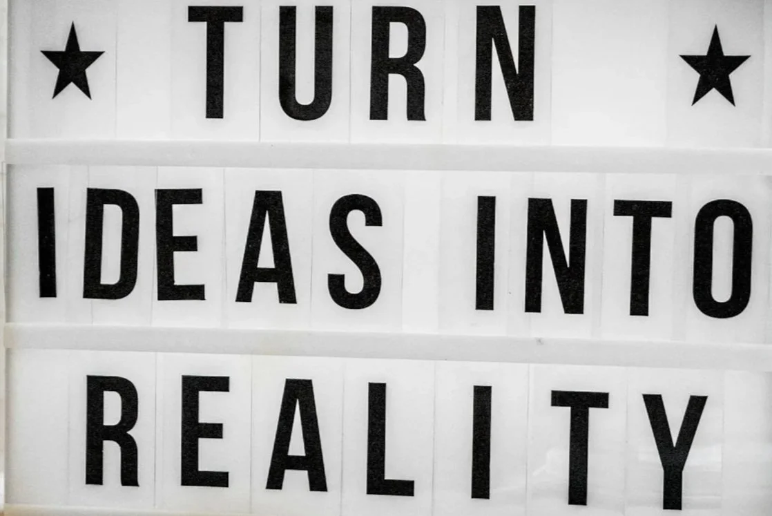 A marquee sign with black letters on a white background displaying the message: "TURN IDEAS INTO REALITY" with star symbols on either side of the word "TURN".