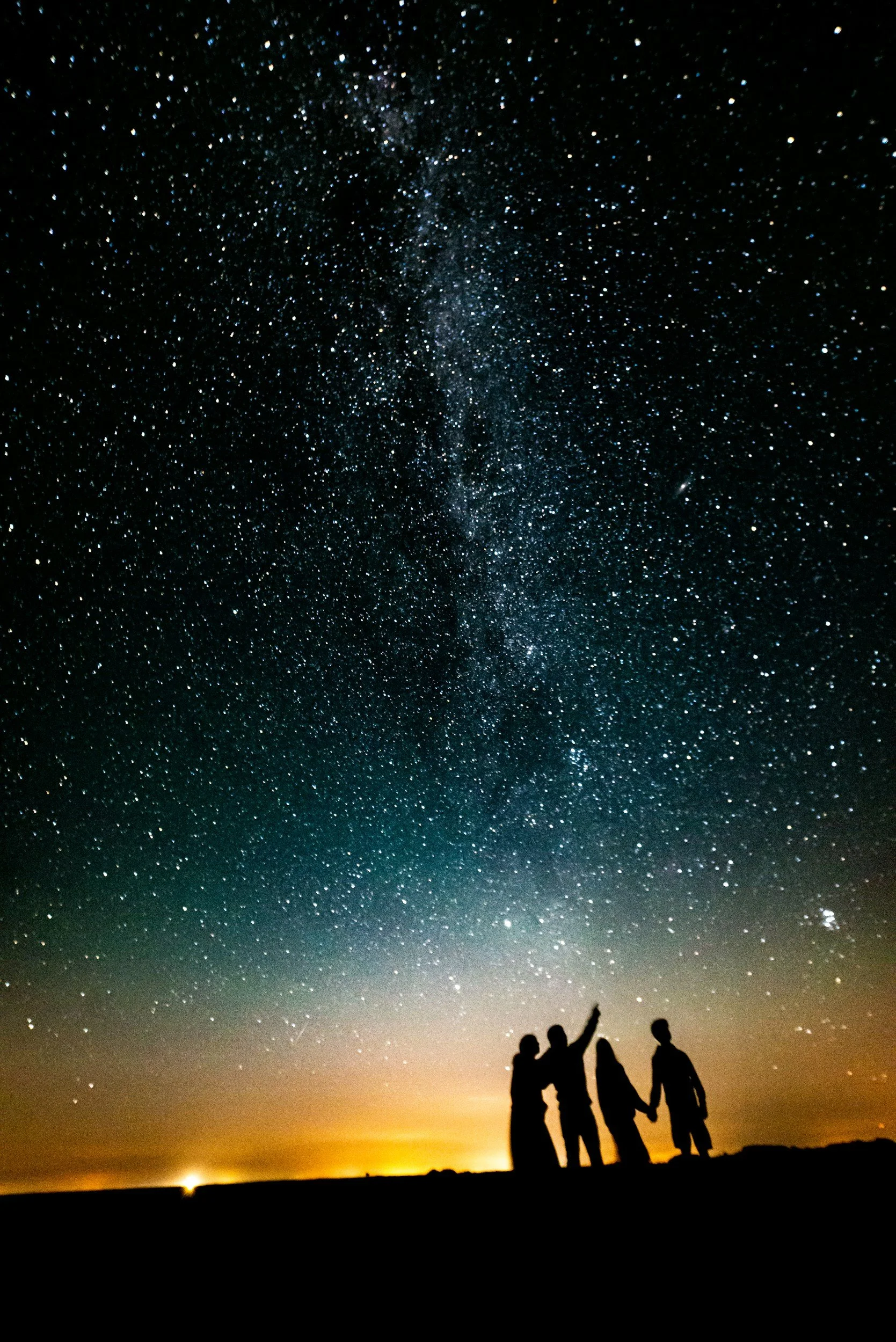 Silhouettes of four people holding hands and standing on a hilltop under a starry night sky with the Milky Way galaxy visible.