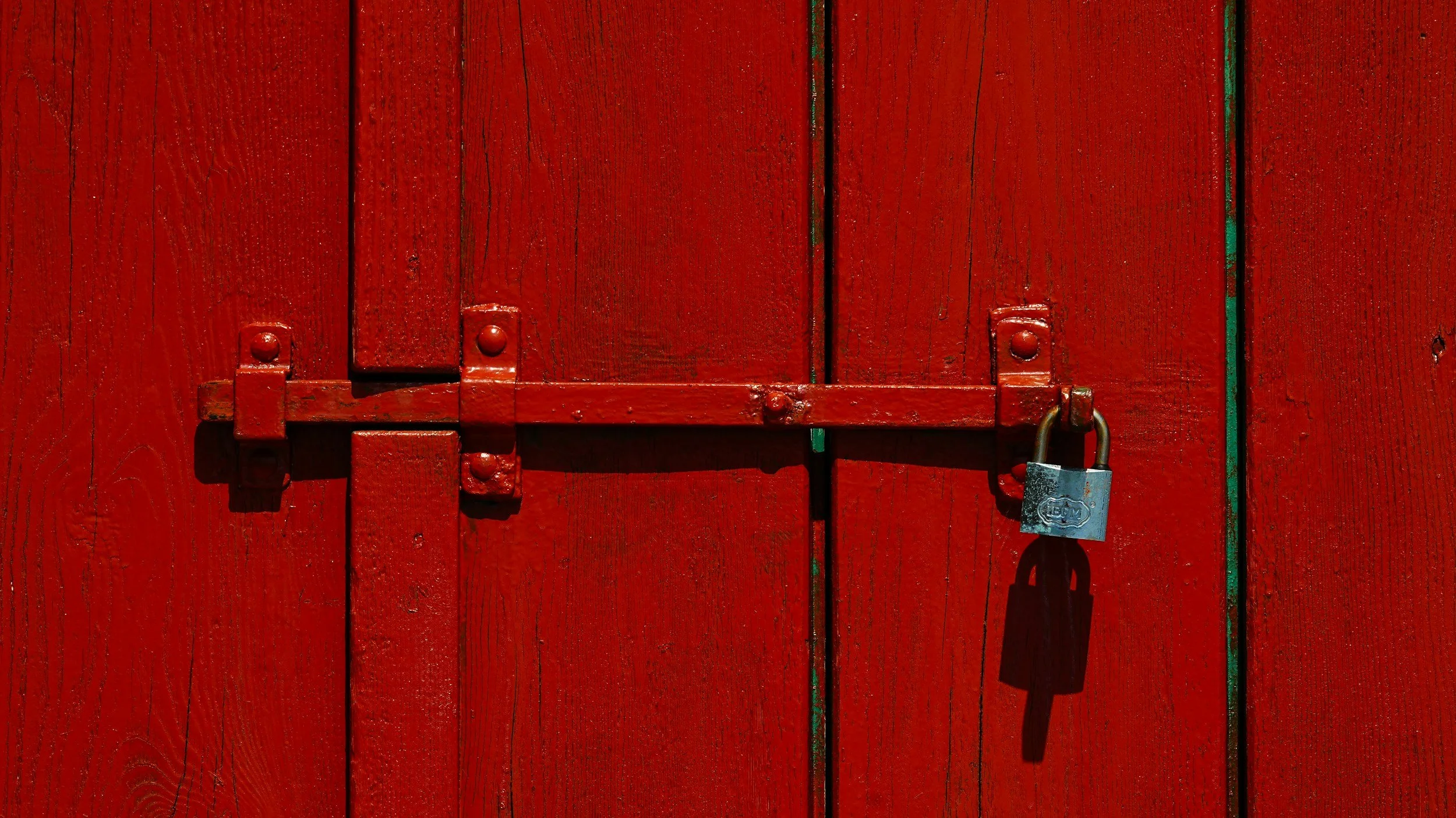 A close-up of a red wooden door with vertical panels, secured by a metal latch and padlock.