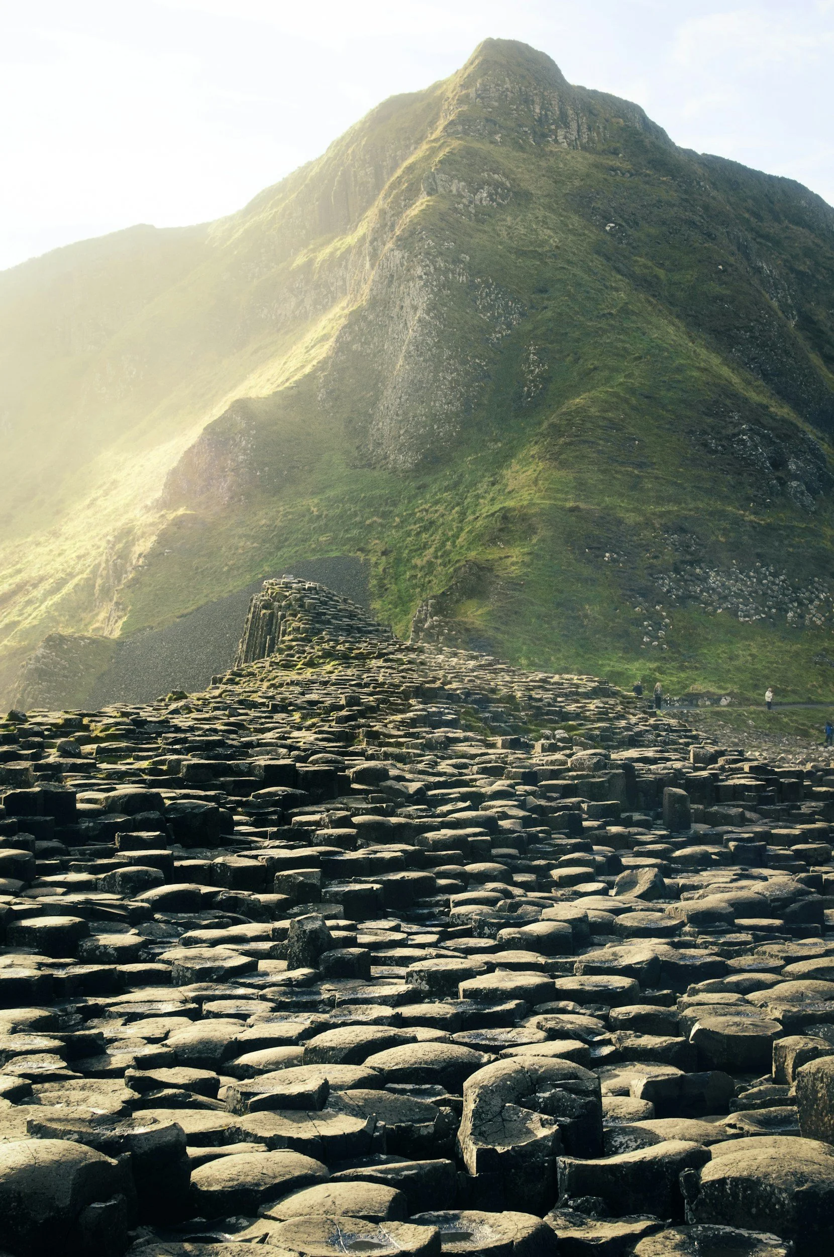 Close-up view of the Giant's Causeway's basalt column formations with a green, mountainous landscape in the background under a cloudy sky.