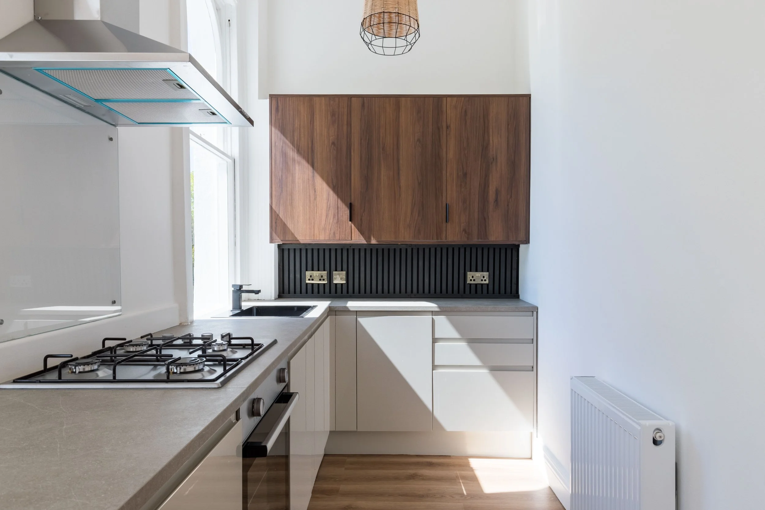 Modern kitchen with white cabinets, a gas stove, a black backsplash, a wooden cabinet above the counter, and a radiator on the right wall.