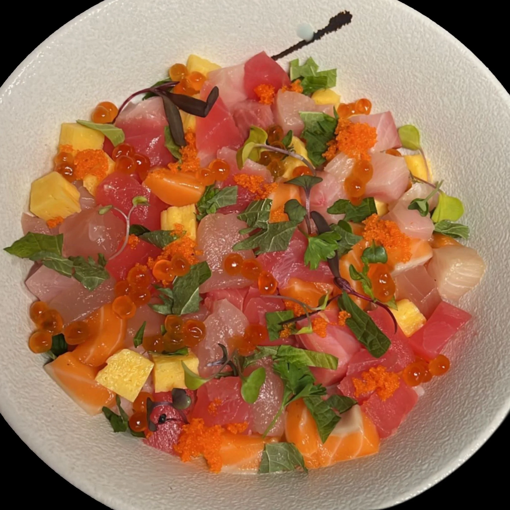 A white plate with slices of raw fish or sashimi, garnished with green herbs, orange fish roe, and small orange and yellow fruit or vegetable pieces.