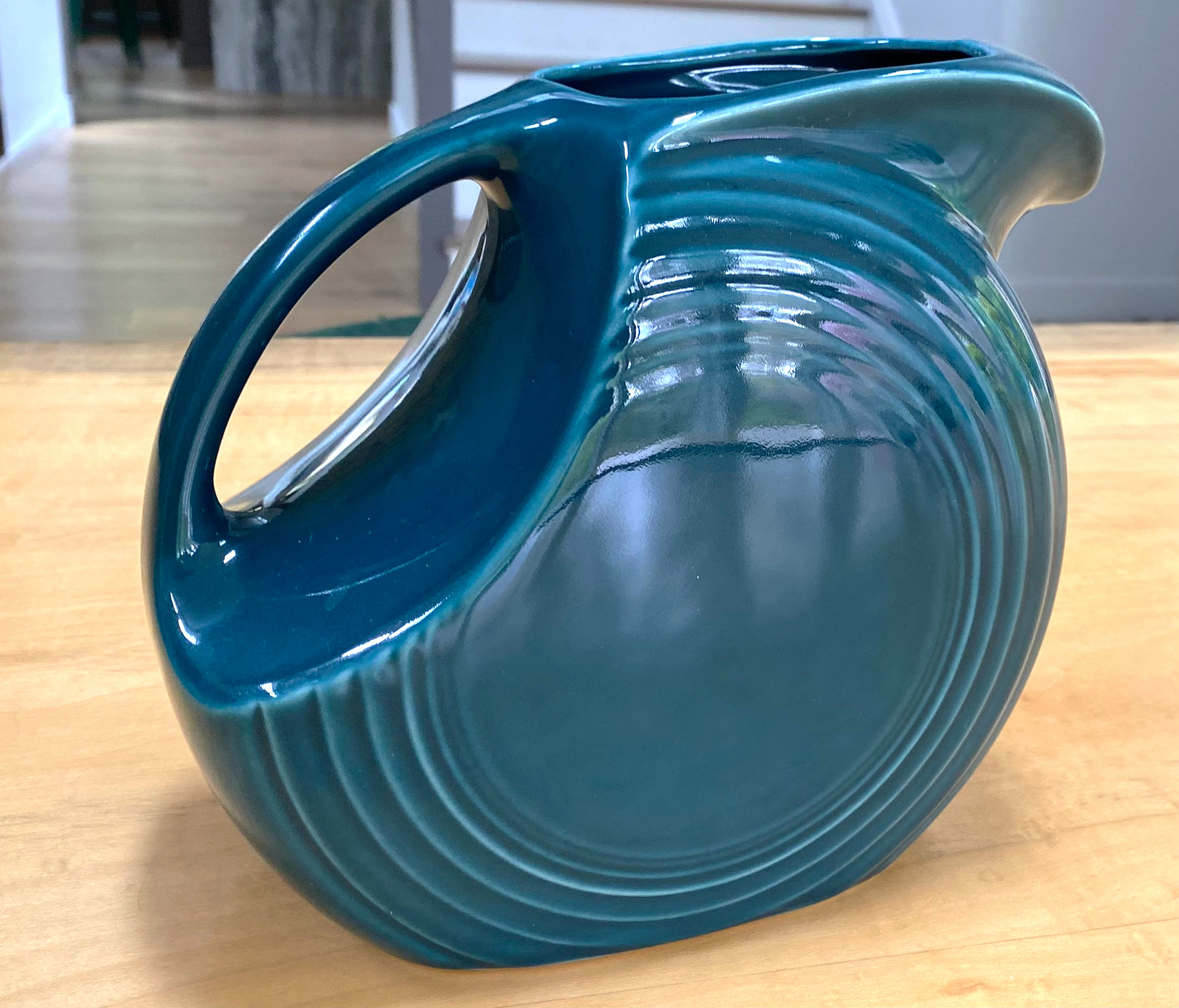 Close-up of a vintage Fiesta Large Disc Pitcher in the juniper glaze - a blue glass art piece with a swirling, layered design, placed on a wooden table