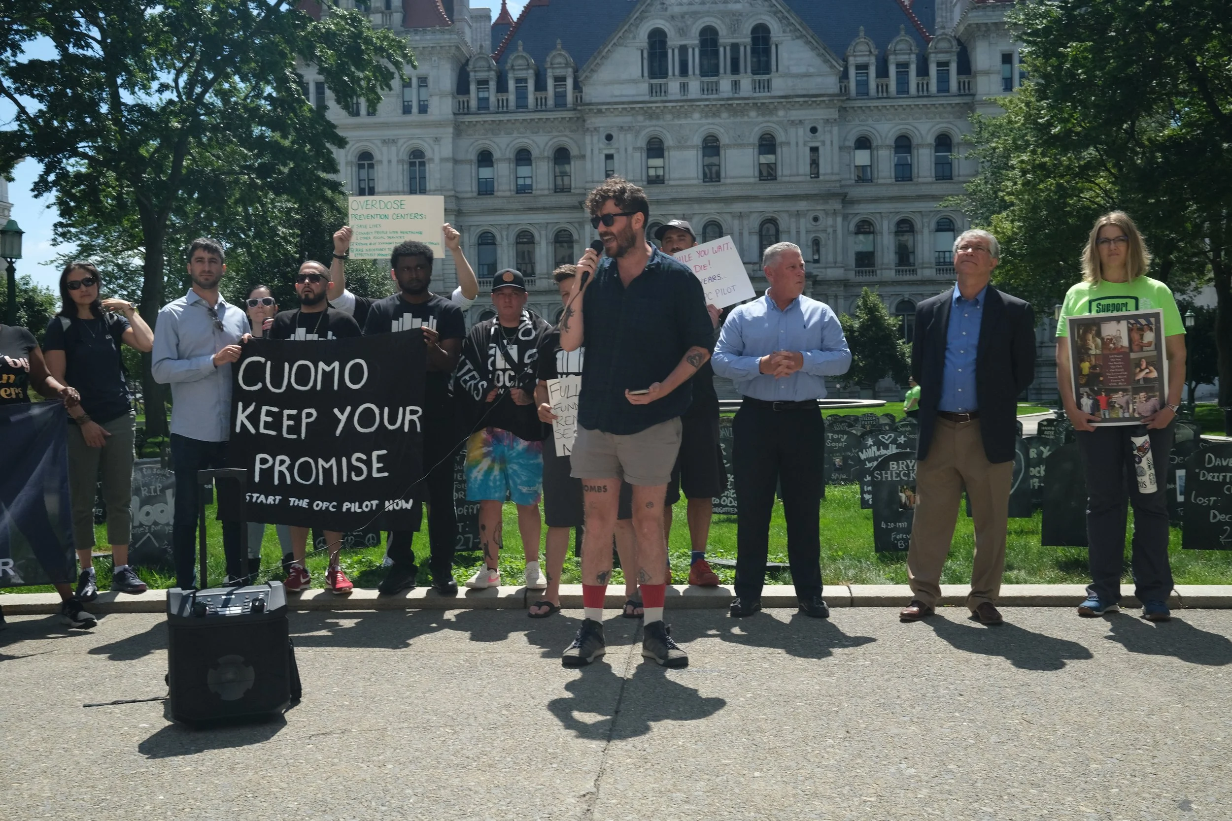 A rally for Overdose Prevention Centers in front of the Governor's Mansion in Albany, New York. Coalition members hold up a large banner that says "Cuomo Keep Your Promise: Start the OPC Pilot Now."