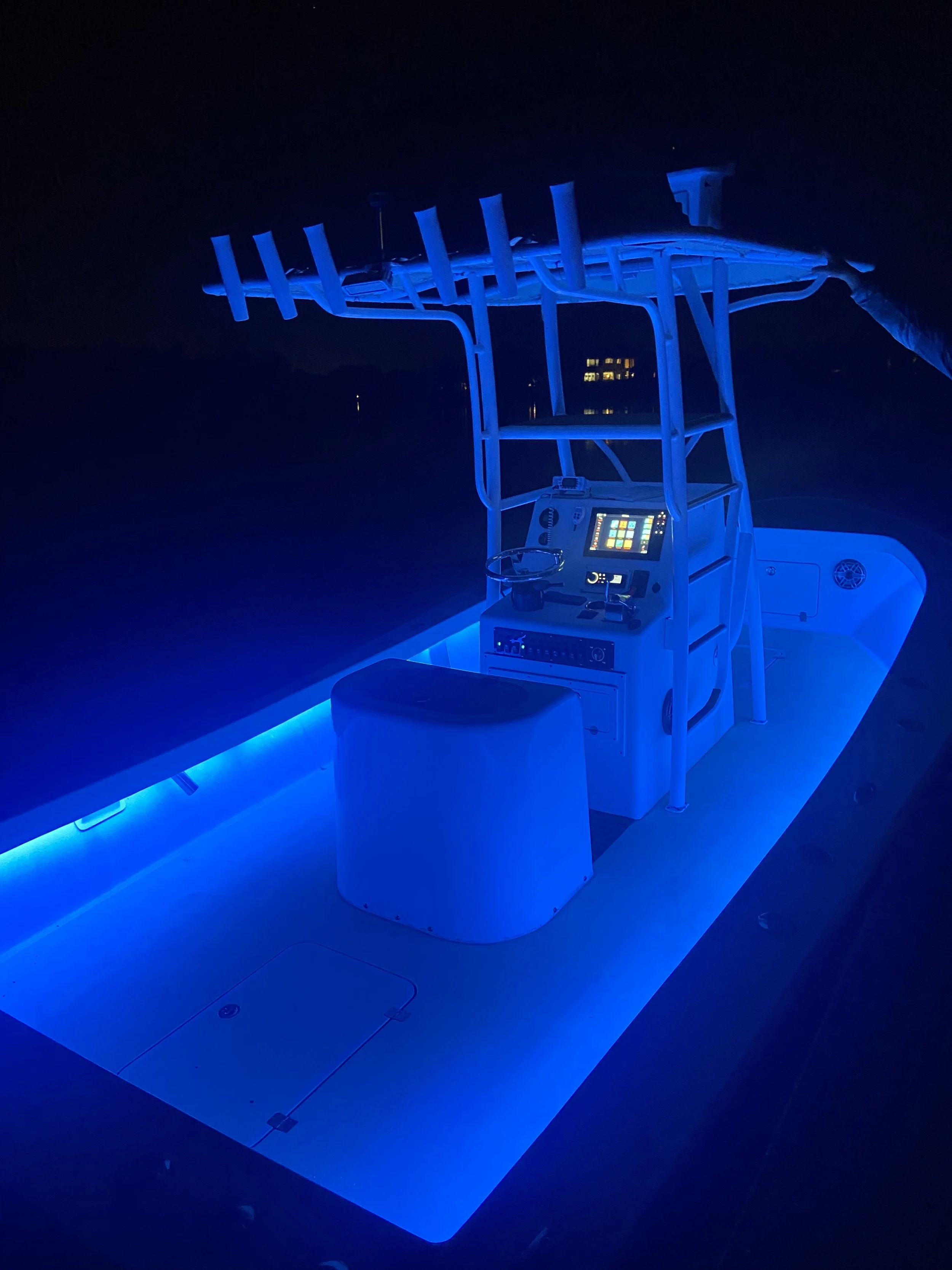 A boat with a large antenna structure illuminated with blue lights at night, with water and city lights in the background.