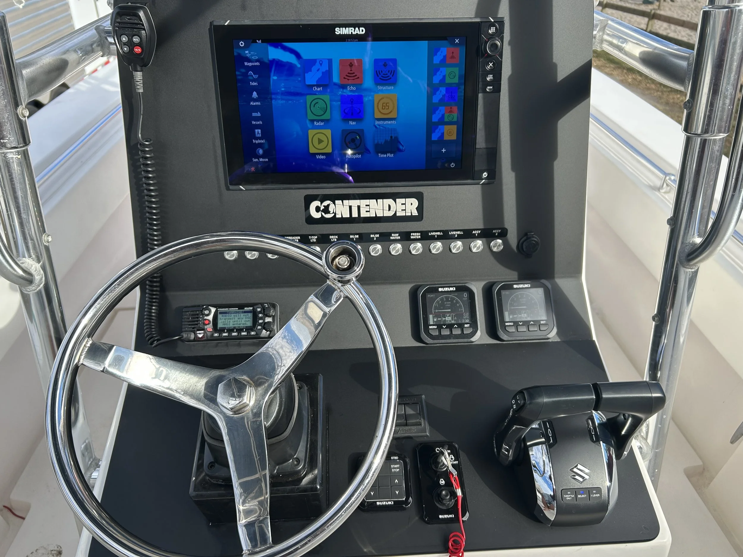 The image shows the helm of a boat with a digital navigation and control system, including a Simrad display screen, various switches, and a steering wheel, all mounted on a dashboard labeled 'Contender'.