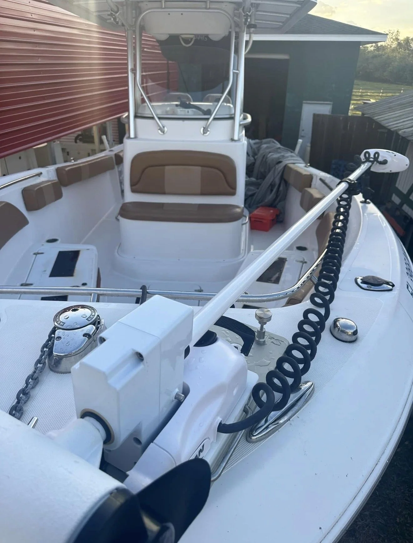 A small fishing boat with seating and equipment, docked near a shed on a sunny day.