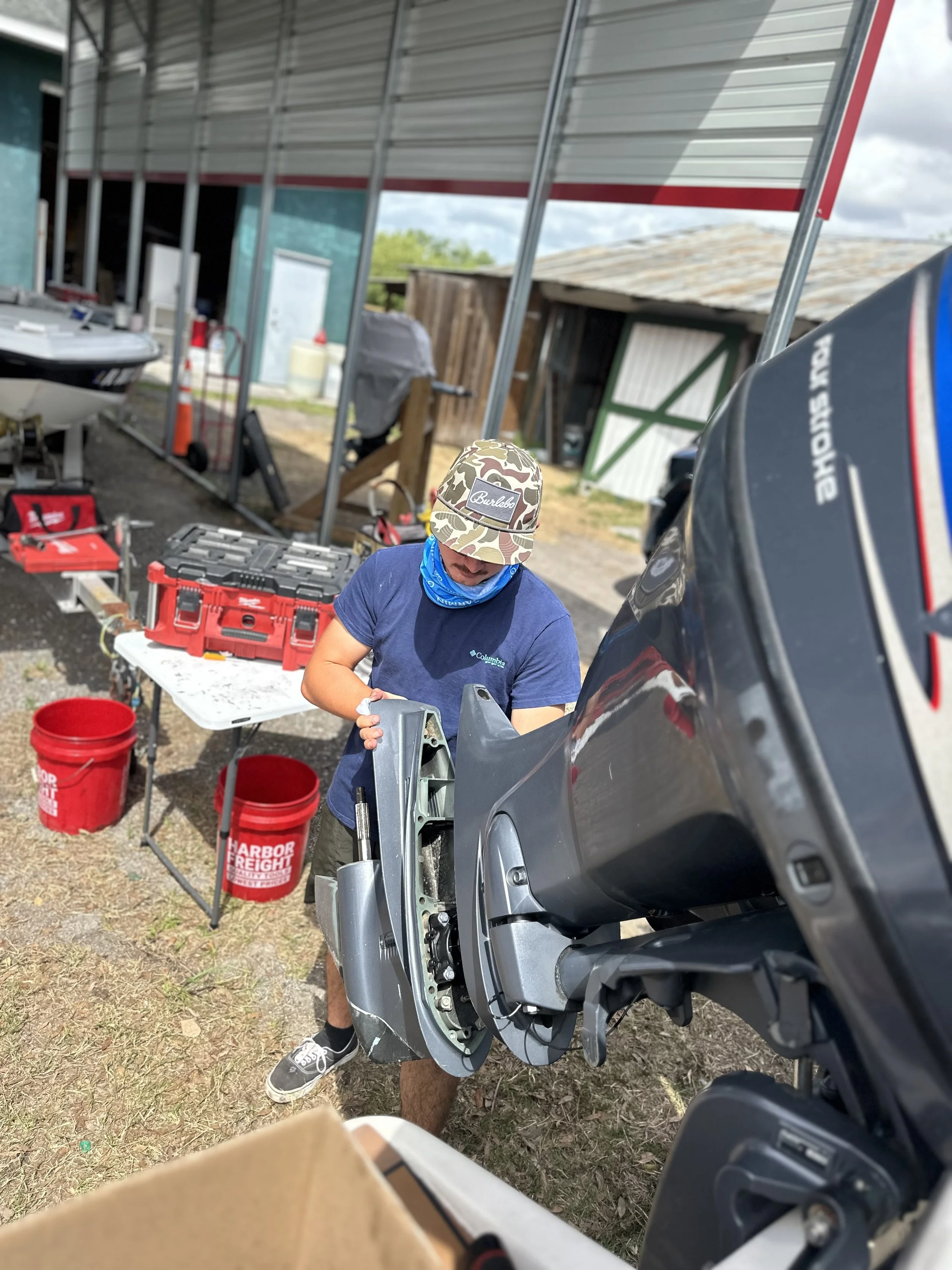 A man working on a motorcycle trailer frame with tools and equipment nearby outdoors.