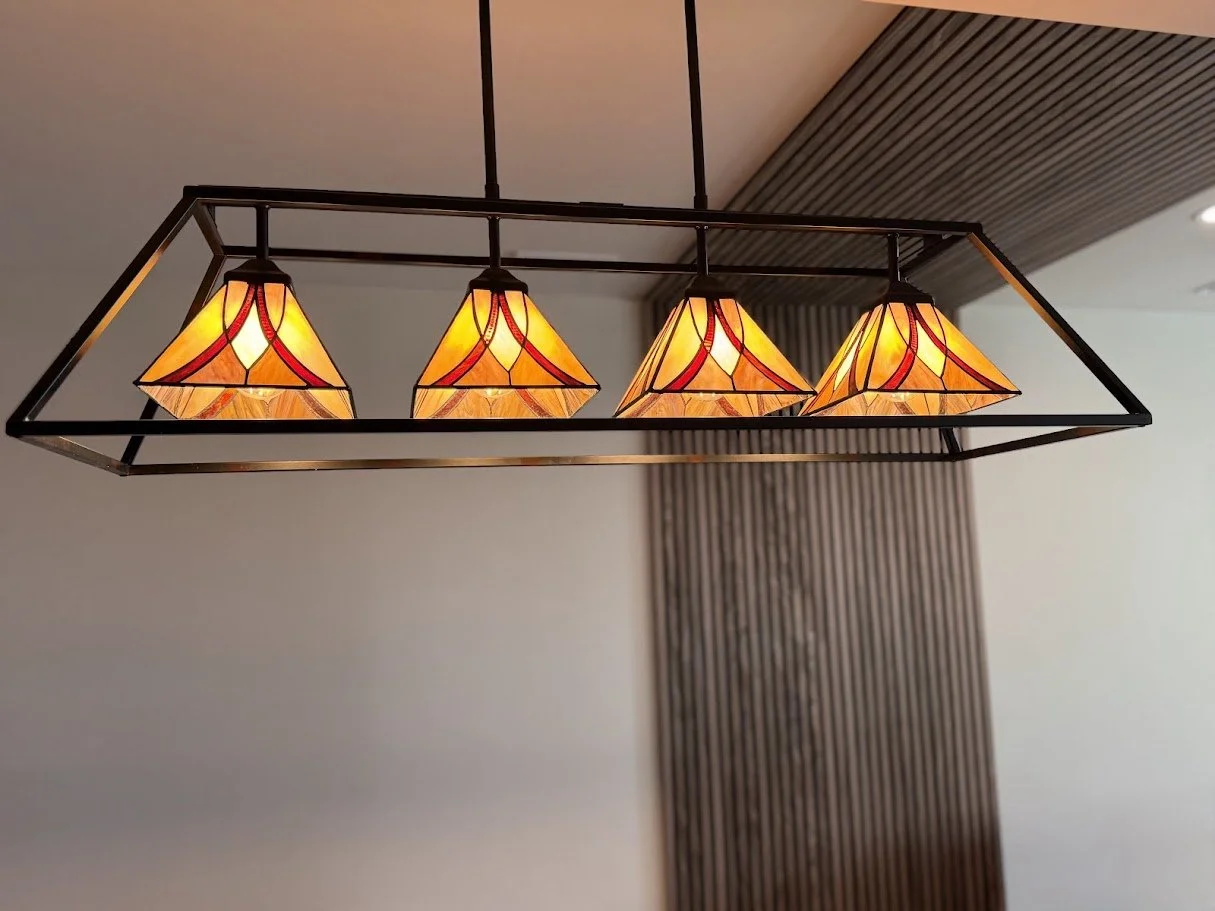 A rectangular chandelier with four stained glass lampshades hanging from the ceiling in a modern interior.