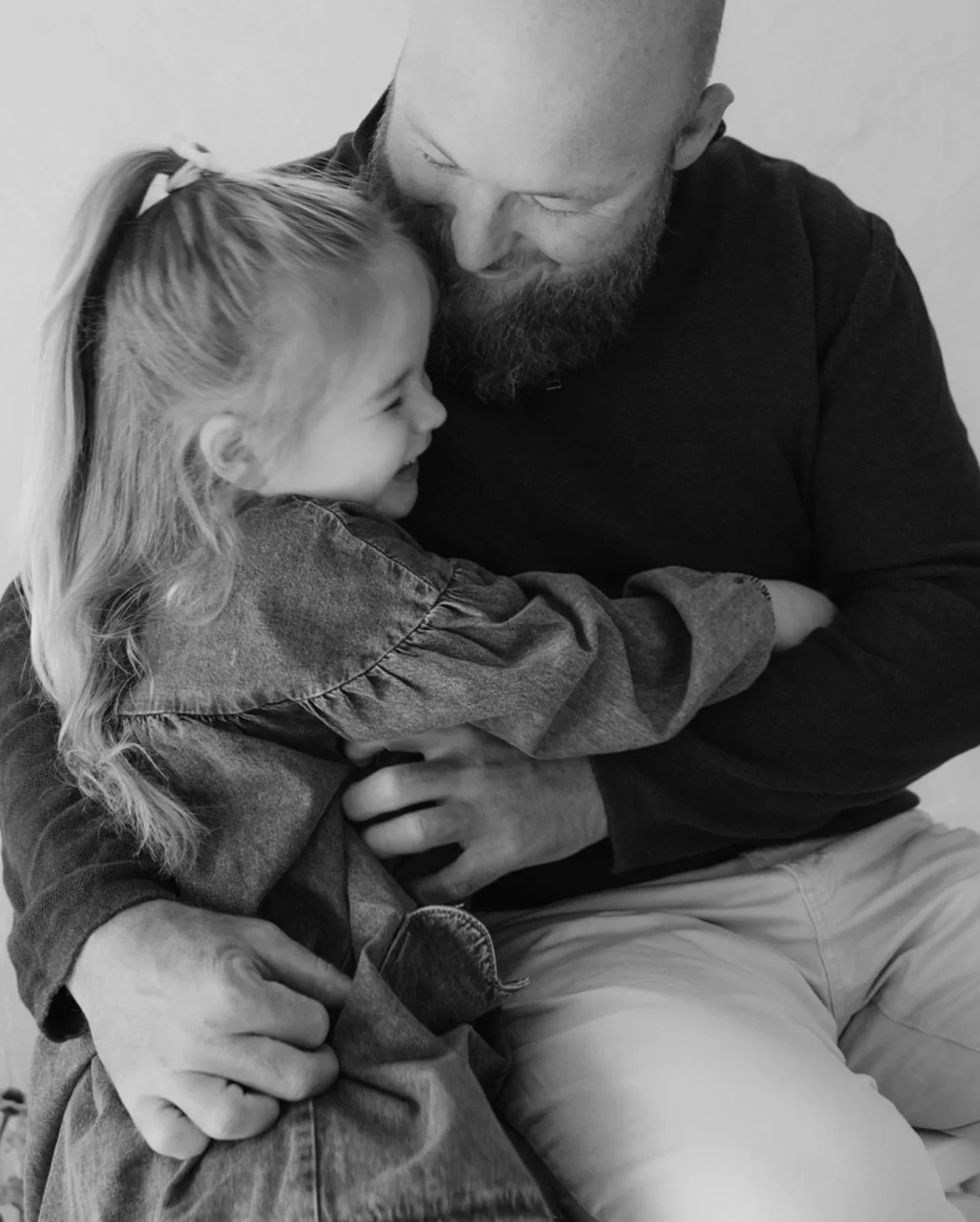 A man with a beard and a young girl hugging and smiling at each other.