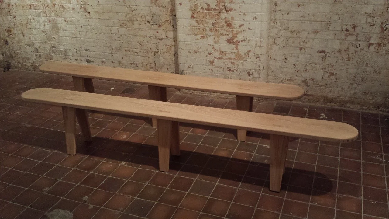 Two wooden benches with rounded edges in front of a brick wall.