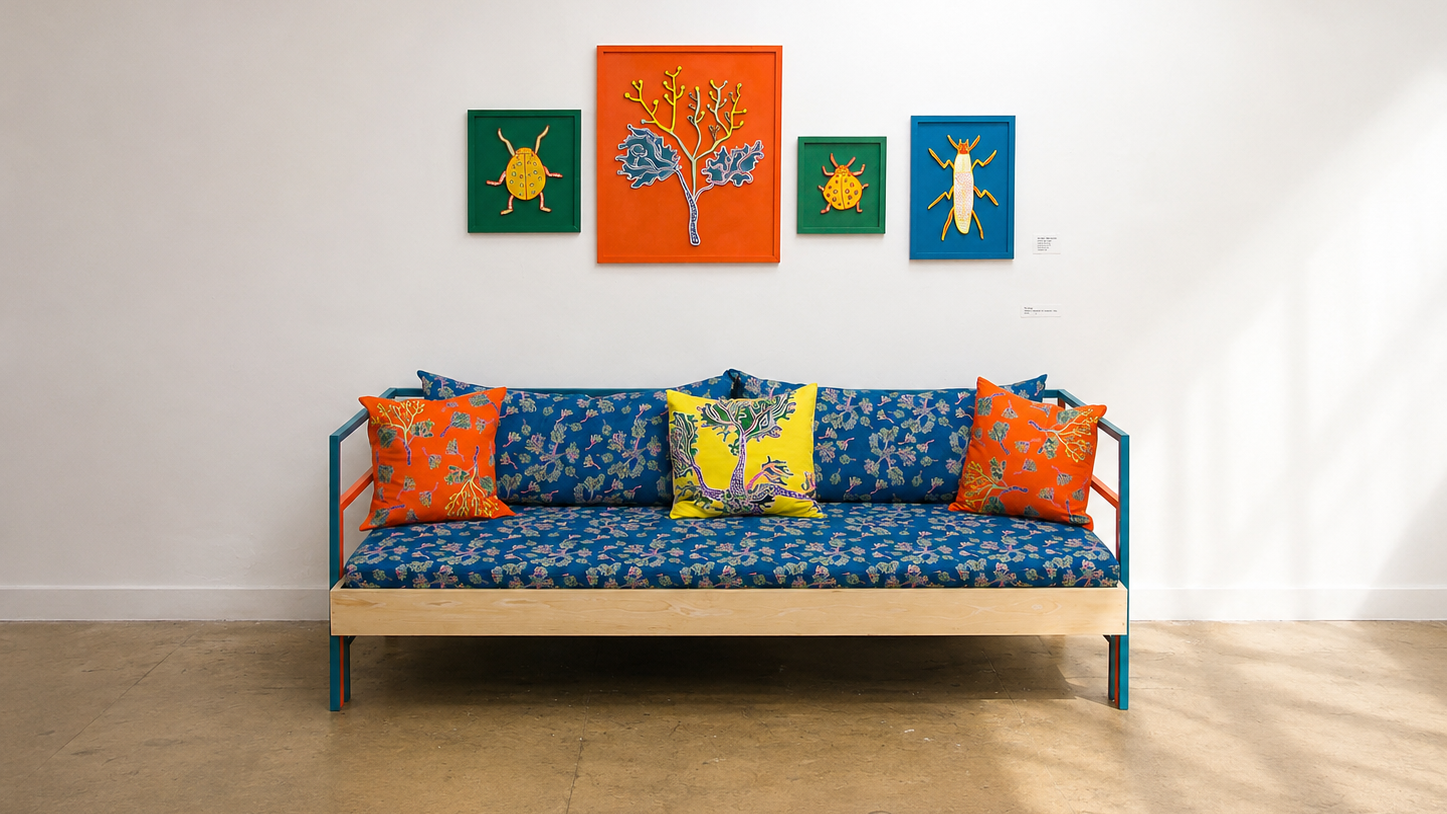 Colorful art gallery with a blue patterned sofa, orange, yellow, and blue pillows, and four framed animal and plant illustrations on the white wall.