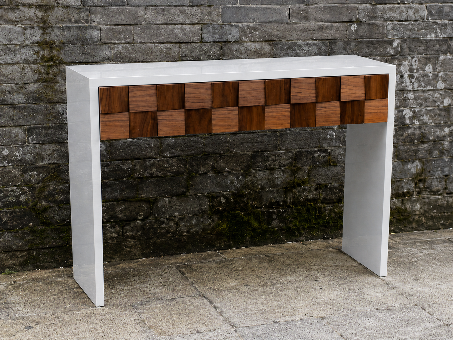Modern console table with a white top, white sides, and a front drawer with a checkerboard pattern of wood squares, placed outdoors against a brick wall.