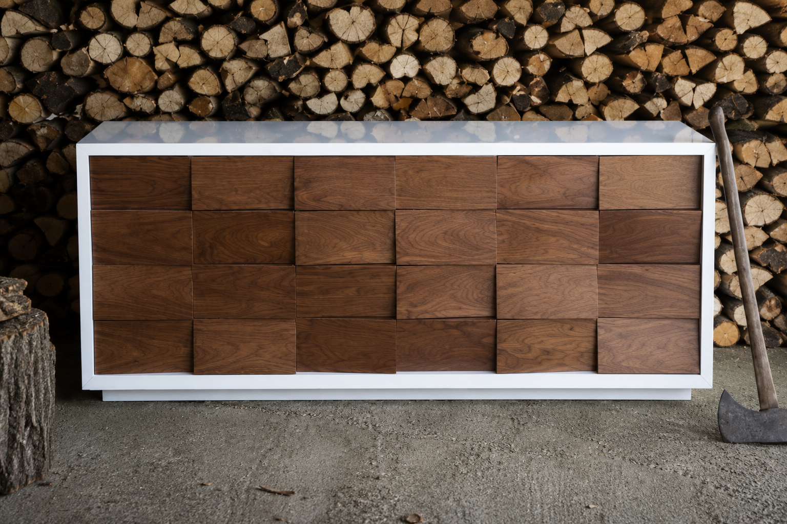 A modern wooden sideboard with a white frame against a background of stacked firewood and a chopping axe on the ground.