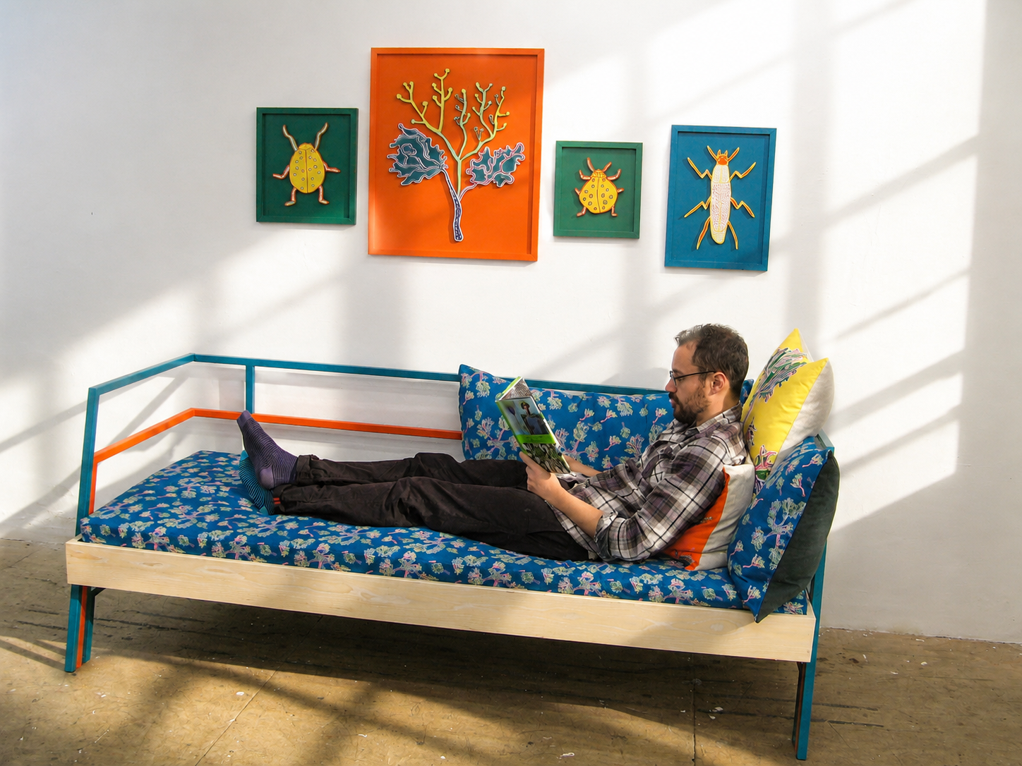 Man relaxing on a colorful bed reading a magazine in a room with abstract animal art hanging on the wall.