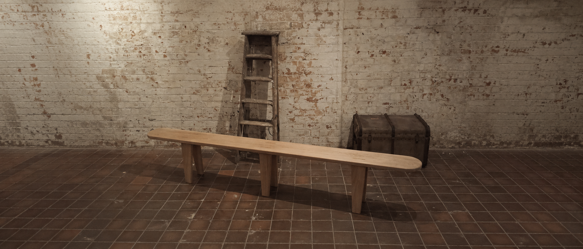 An interior space with a white brick wall, a wooden bench, a rustic wooden ladder, an old storage trunk, and a tiled floor.