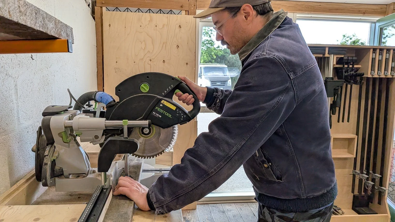A man cutting a piece of wood using a sliding miter saw in a woodworking shop.