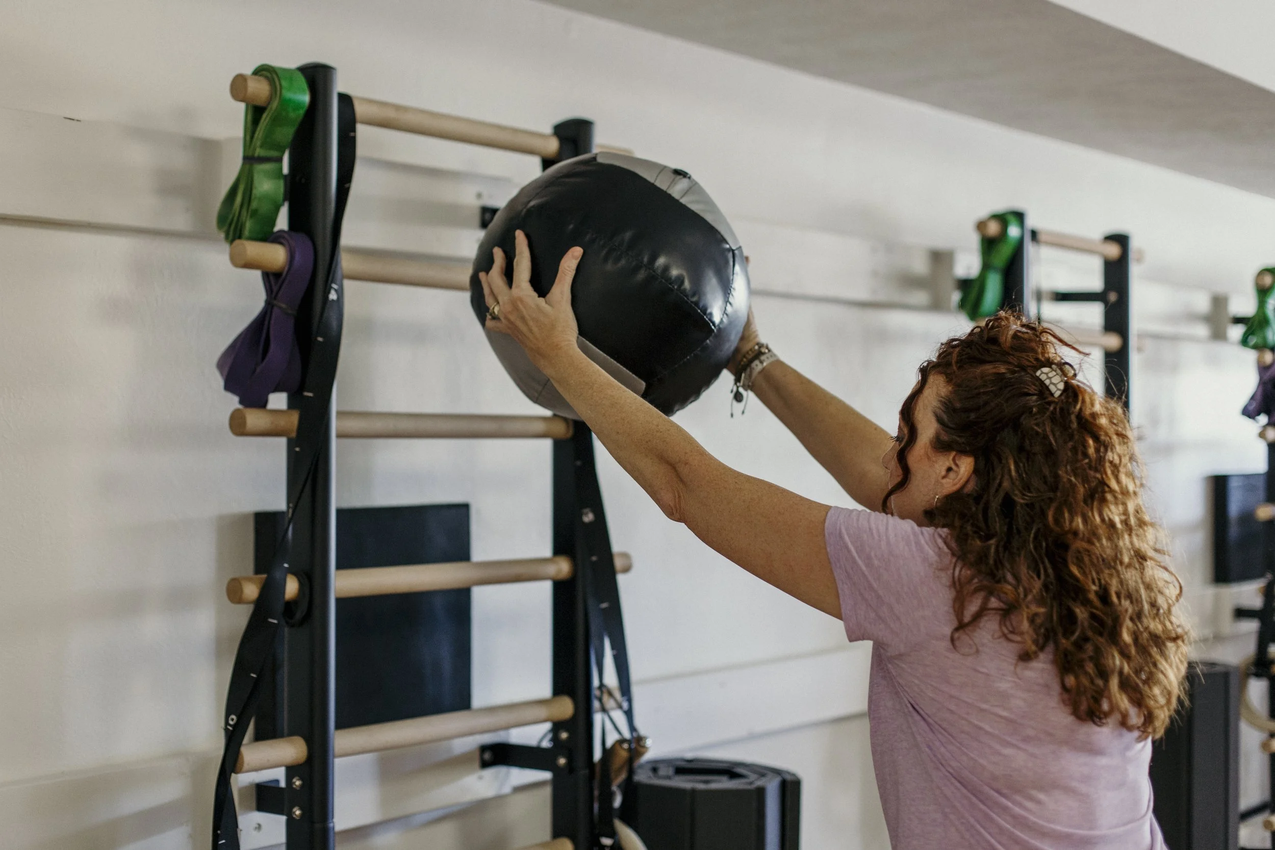 Woman lifting a medicine ball toward the wall during a personal training session.