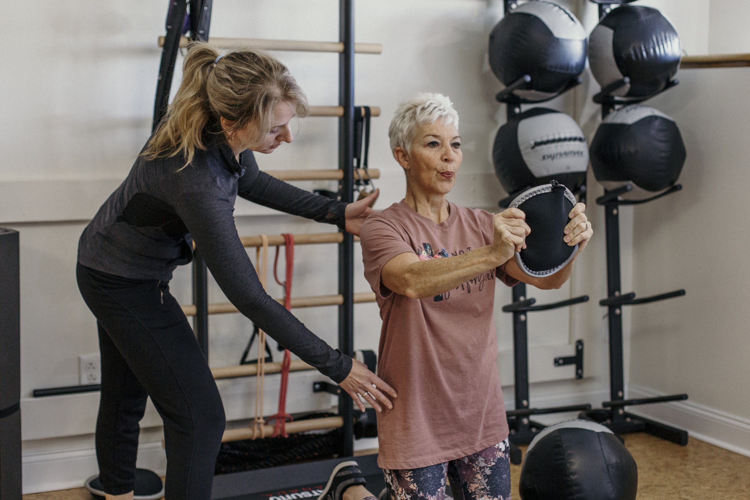 Personal trainer guiding a woman through a strength exercise using a weighted bag.
