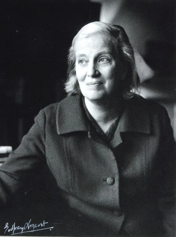 Black-and-white photograph of Dorothy Hodgkin in 1969 with shoulder-length hair, wearing a dark coat, looking to the side with a slight smile.