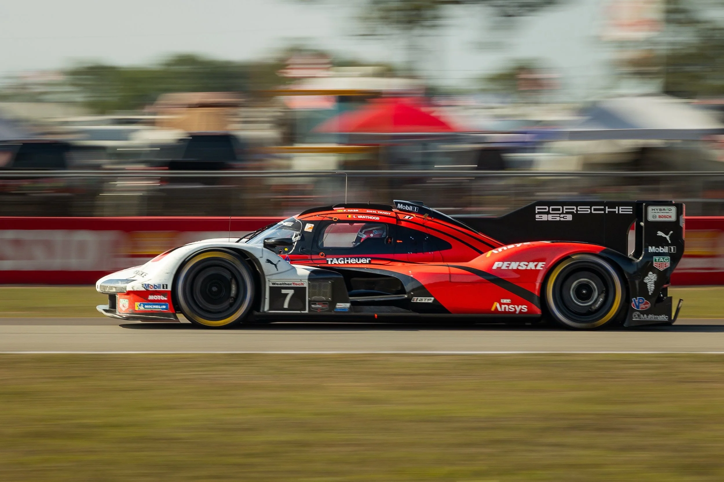 A race car speeding on a track with a motion blur background, decorated with sponsors' logos including Porsche, TAG Heuer, and Mobil 1.