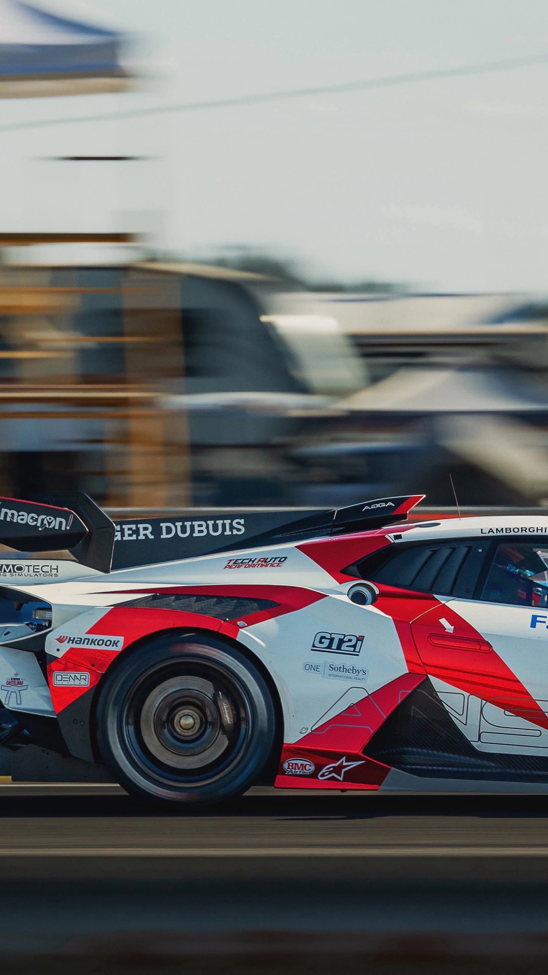 A racing car moving at high speed, with a blurred background, detailed with sponsor logos and a sleek red, white, and black design.