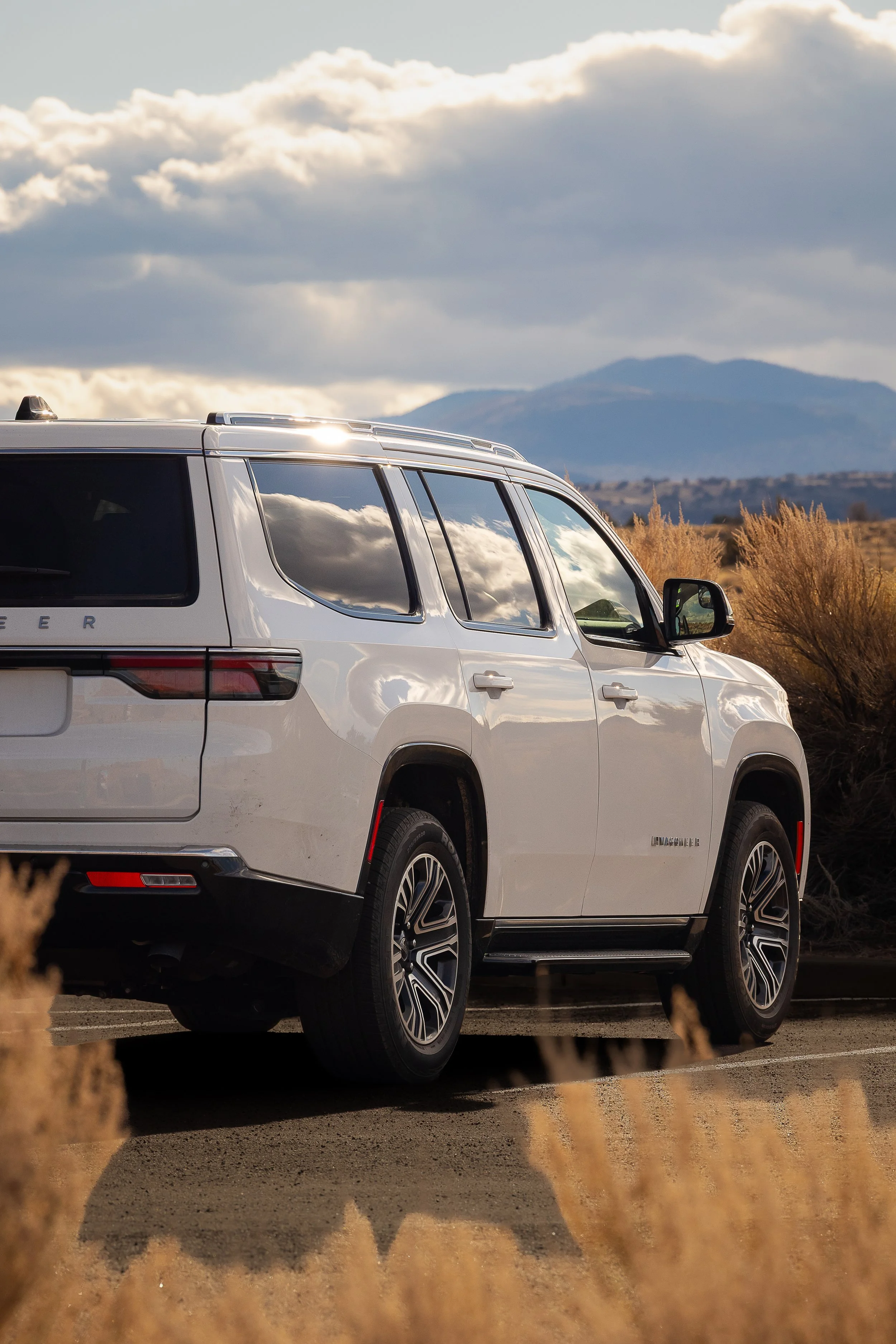 A white SUV parked on a dirt road with mountains in the background and cloudy sky during sunset.