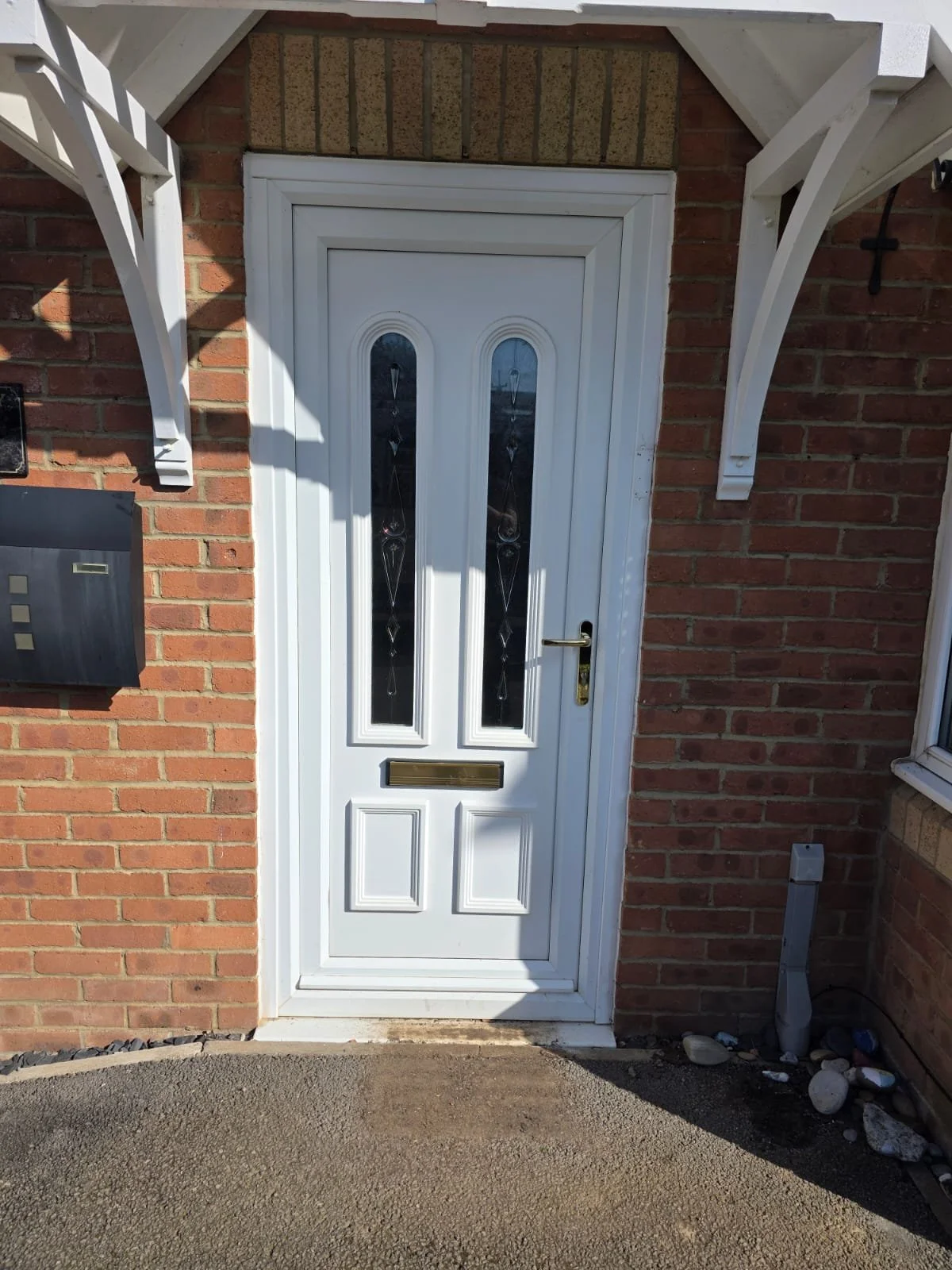 White front door with decorative glass panels, set in a brick wall, with a black mailbox, and a small white box on the ground nearby.