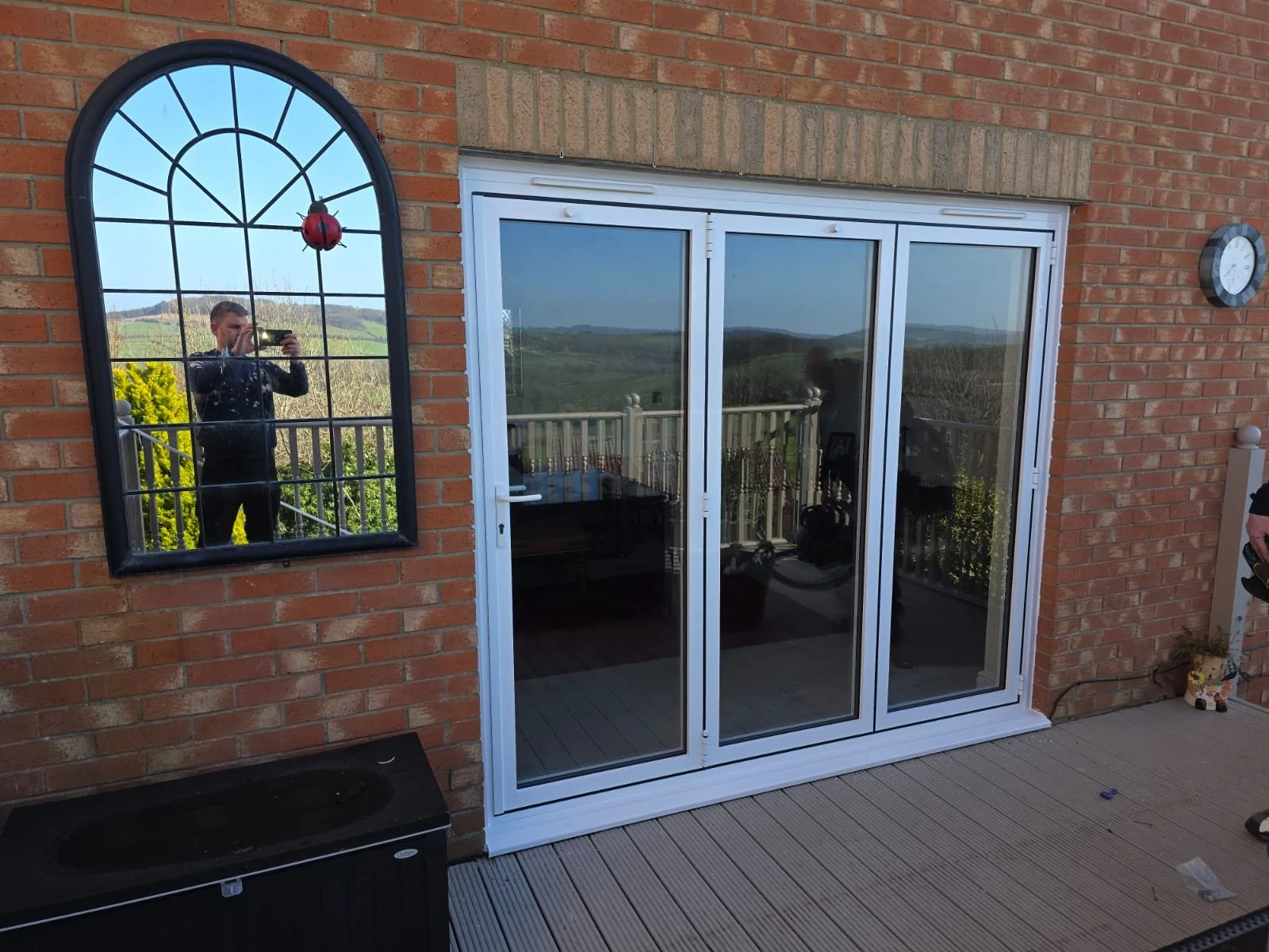 A brick house exterior with a sliding glass door leading to a balcony overlooking a green landscape.
