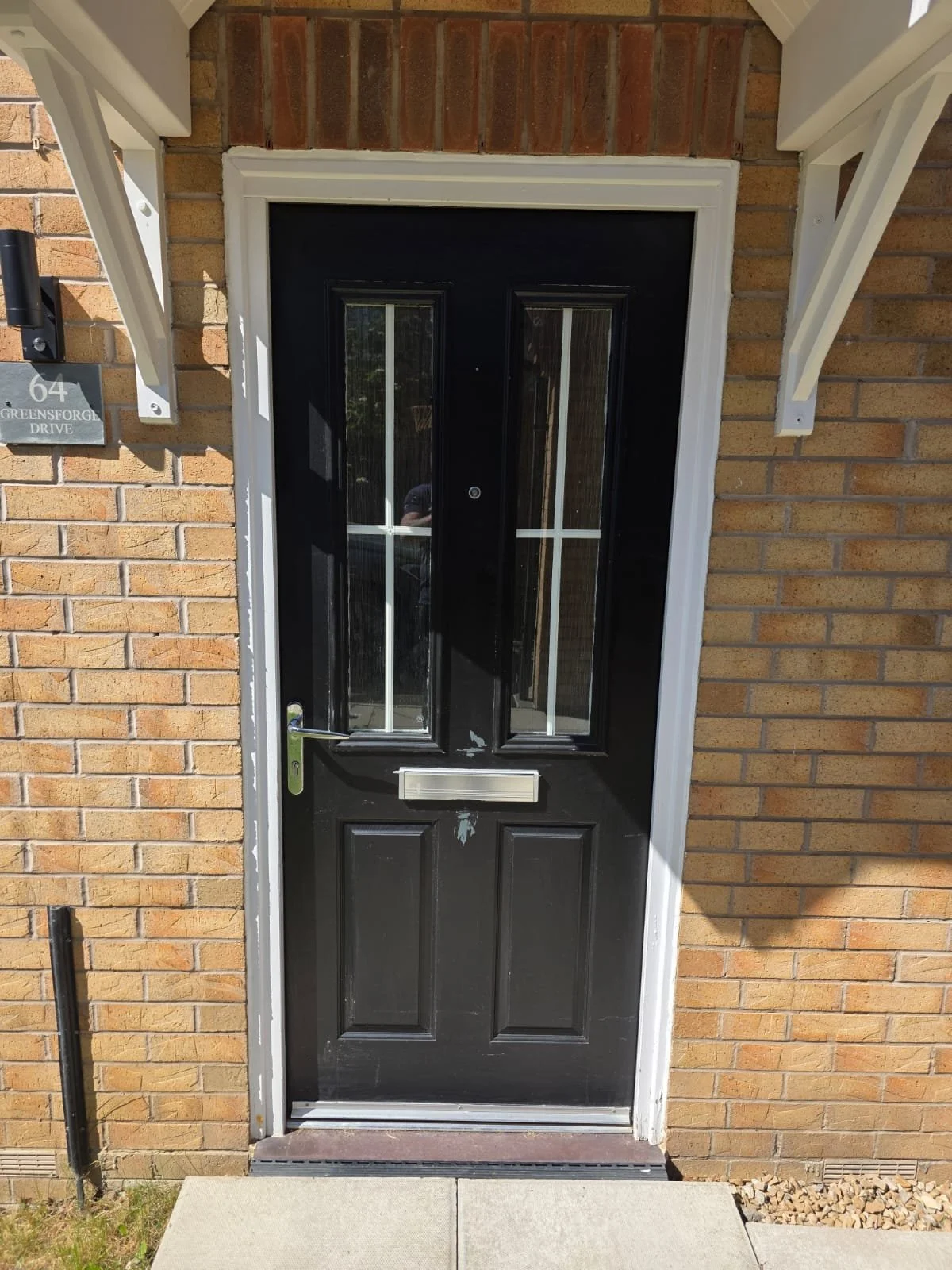 Front door of a brick house painted black with glass panels and a mail slot, surrounded by a white door frame, with a small concrete porch and walkway in front.