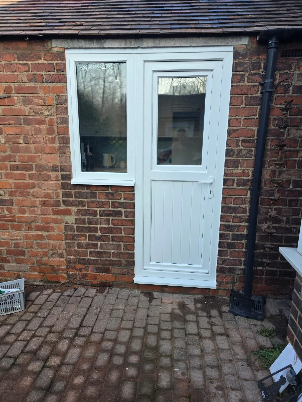 A white glass and plastic door with a window, set in a brick wall, with a black rain gutter pipe running alongside it.