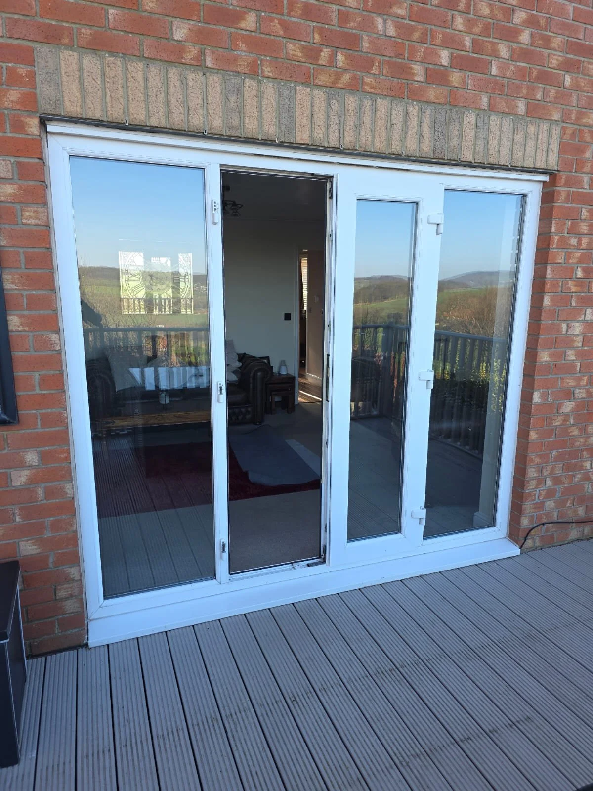 Exterior view of a sliding glass door leading to a balcony with scenic hills and trees in the background.