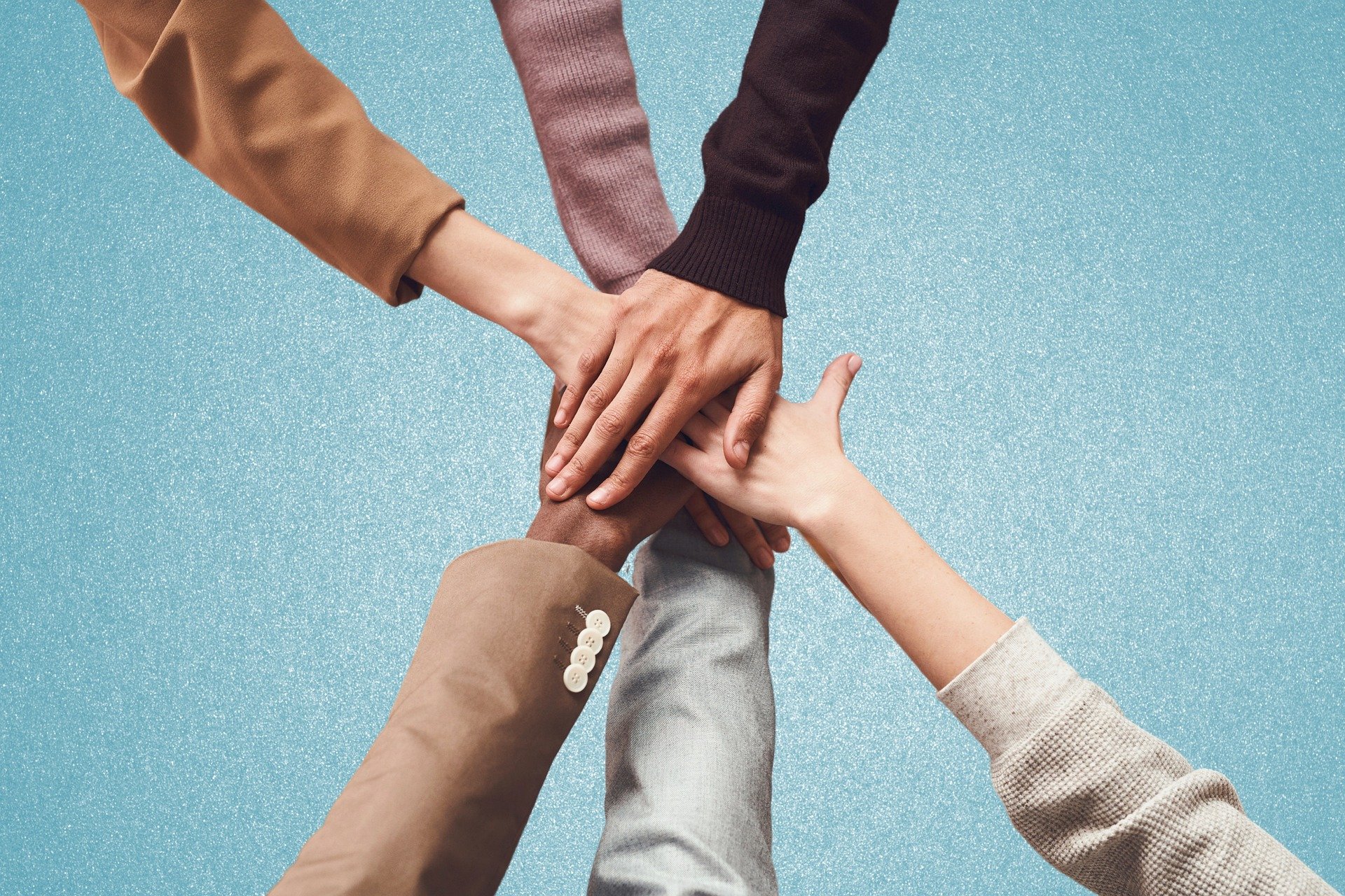 Multiple hands stacked together in a show of unity against a blue glittery background.
