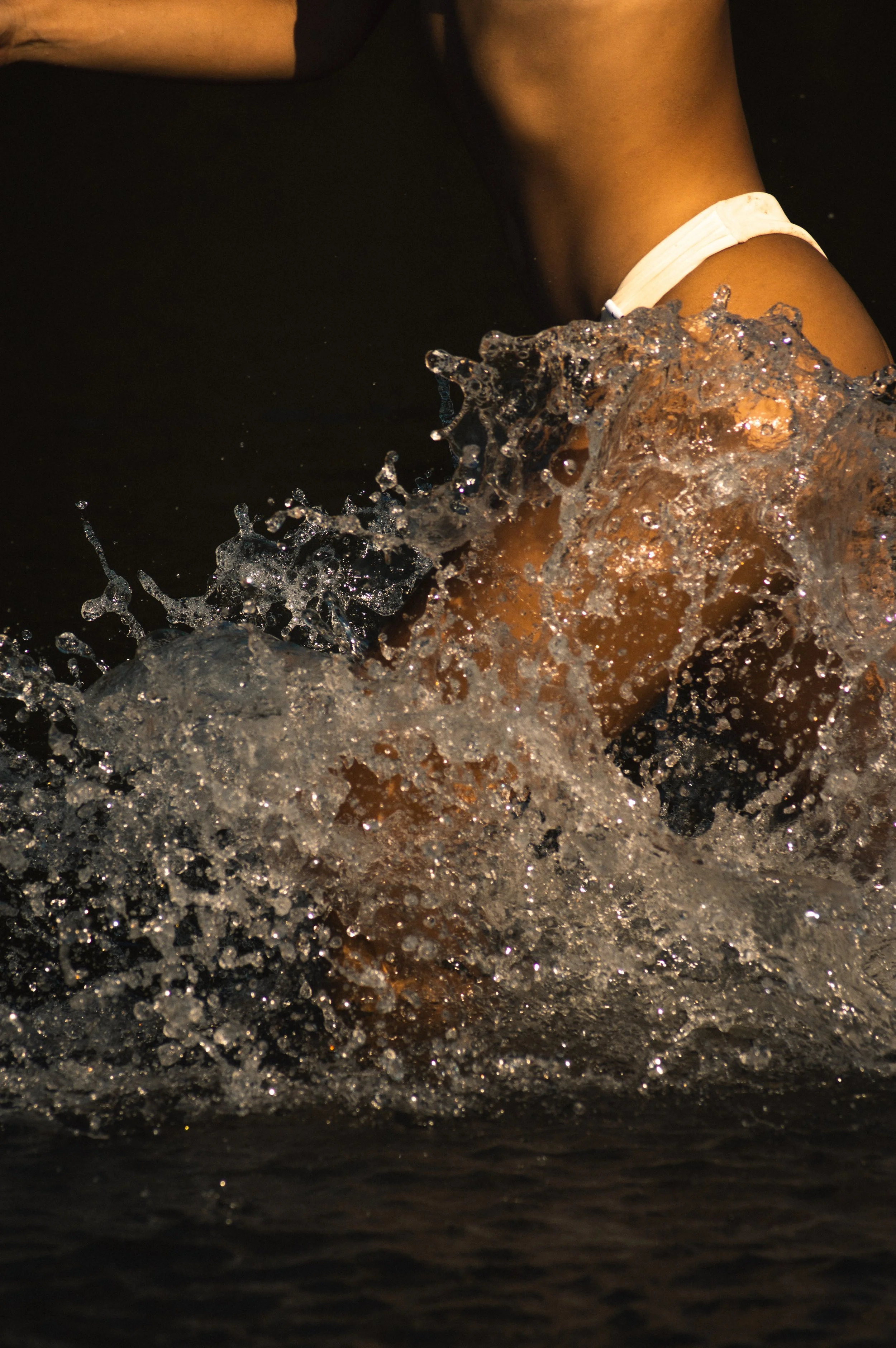 Close-up of a person wearing a black shirt and white shorts, with water splashing around them, creating a dynamic scene.
