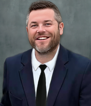 A smiling man in a navy suit with a white shirt and black tie, standing in front of a gray background.