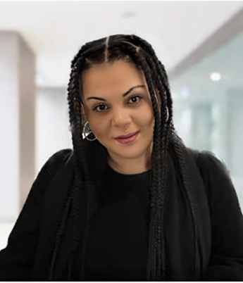 Portrait of a woman with dark braided hair, wearing a black top, smiling subtly in an indoor setting.
