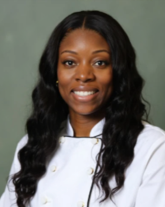 Professional woman with long wavy hair wearing a white chef's coat against a green background.