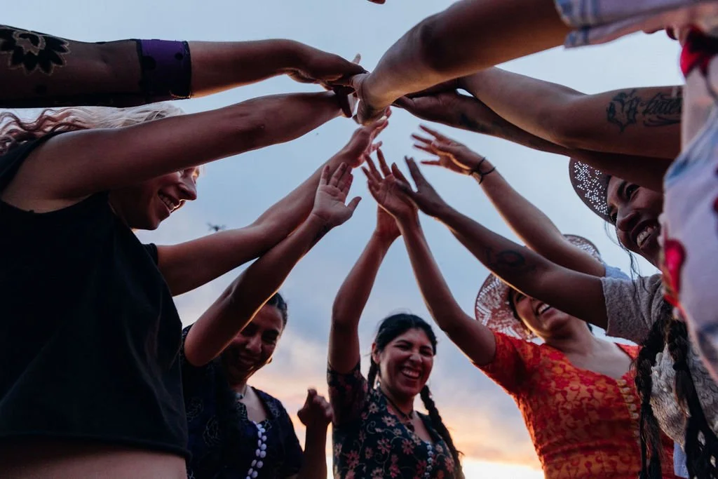 Photo of smiling women coming together in a circle to touch hands in the center