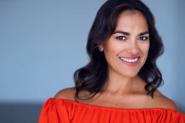 A woman with dark brown hair wearing a red button-up shirt, smiling softly.