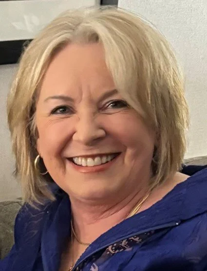 A smiling woman with blonde hair wearing a blue top and gold hoop earrings.