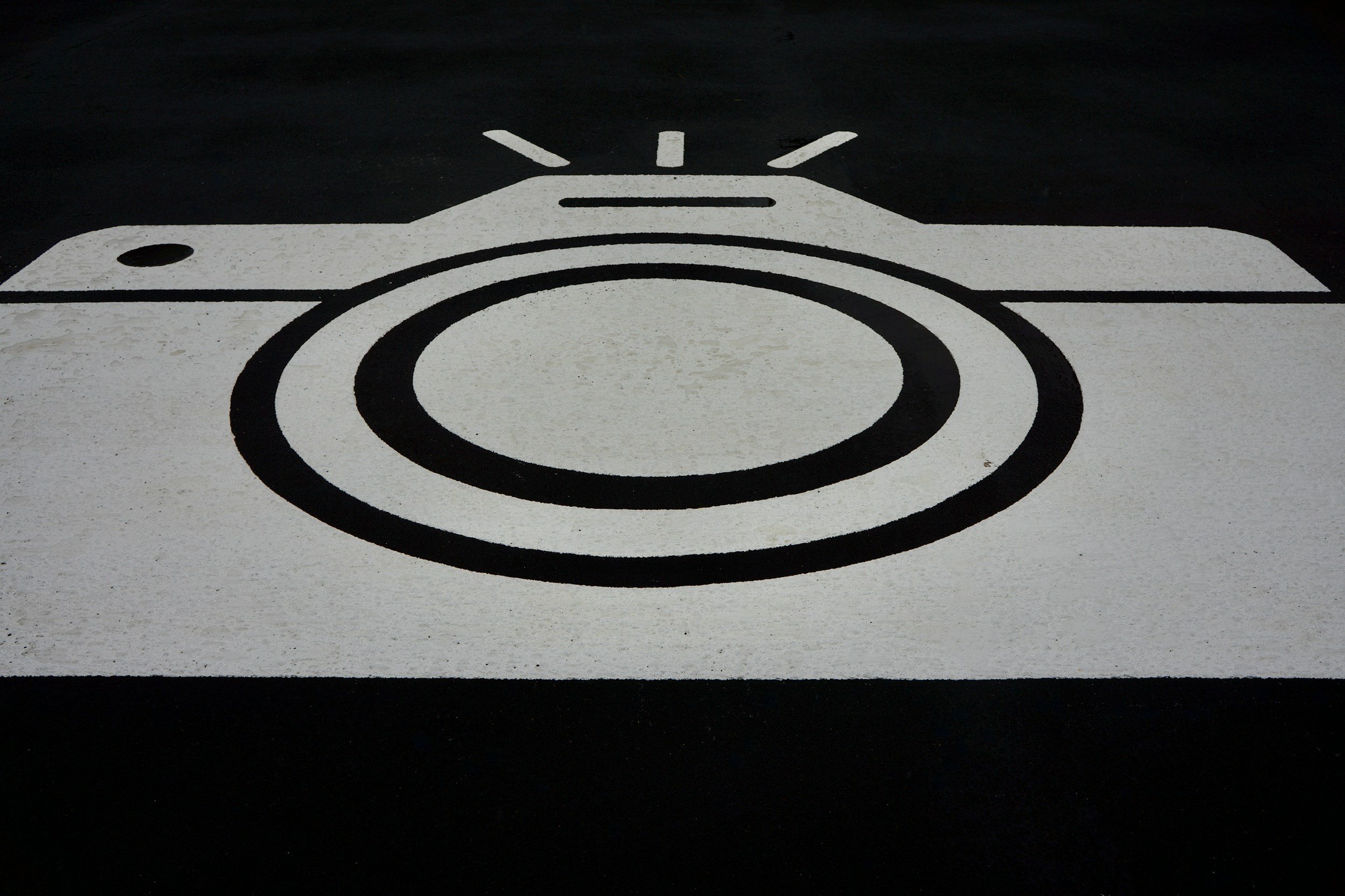 A painted parking space symbolized with a white camera icon on a black background.