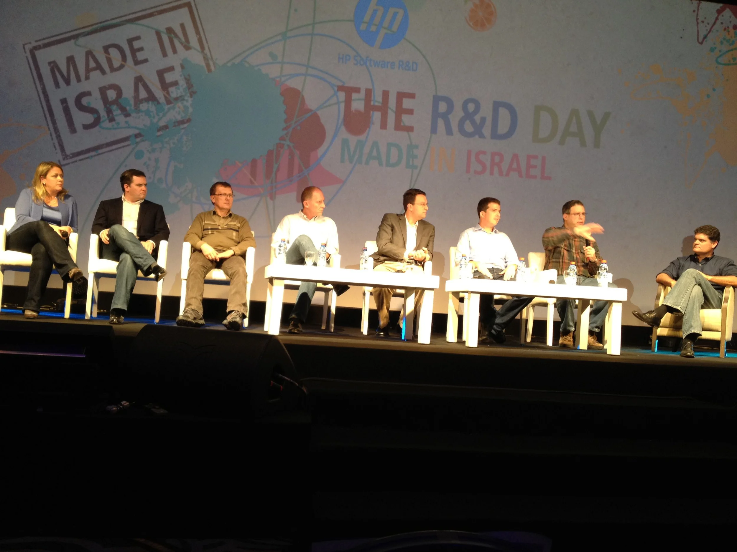 A panel discussion on stage with eight individuals seated in white chairs, and a backdrop with the words 'The R&D Day Made in Israel' along with a map of Israel and logos, including HP.