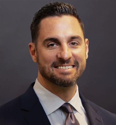 Professional headshot of a man in a suit against a dark background