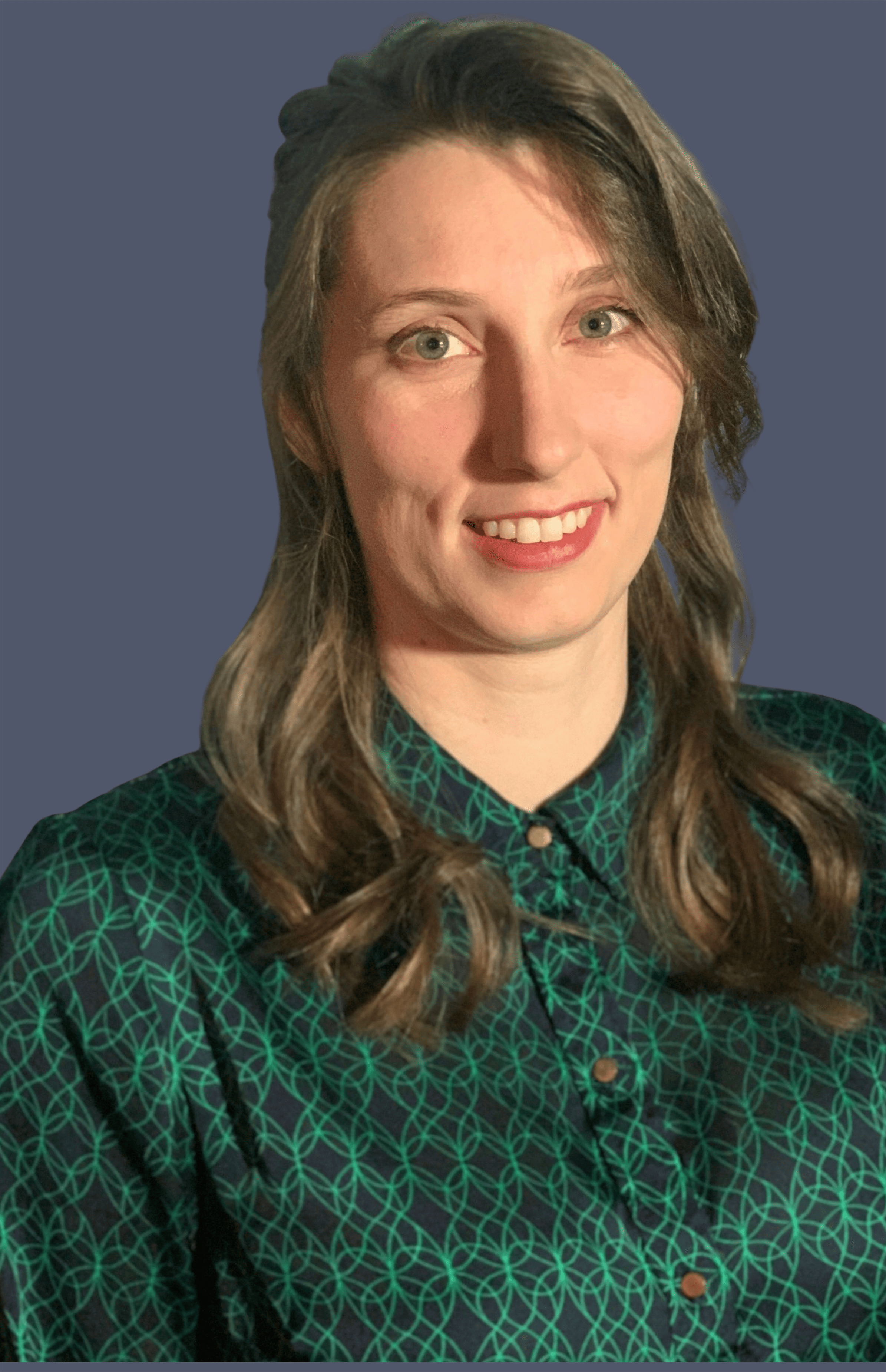 A woman with long, wavy brown hair and light skin, smiling, wearing a green and black patterned blouse with a collar, standing against a plain dark blue background.