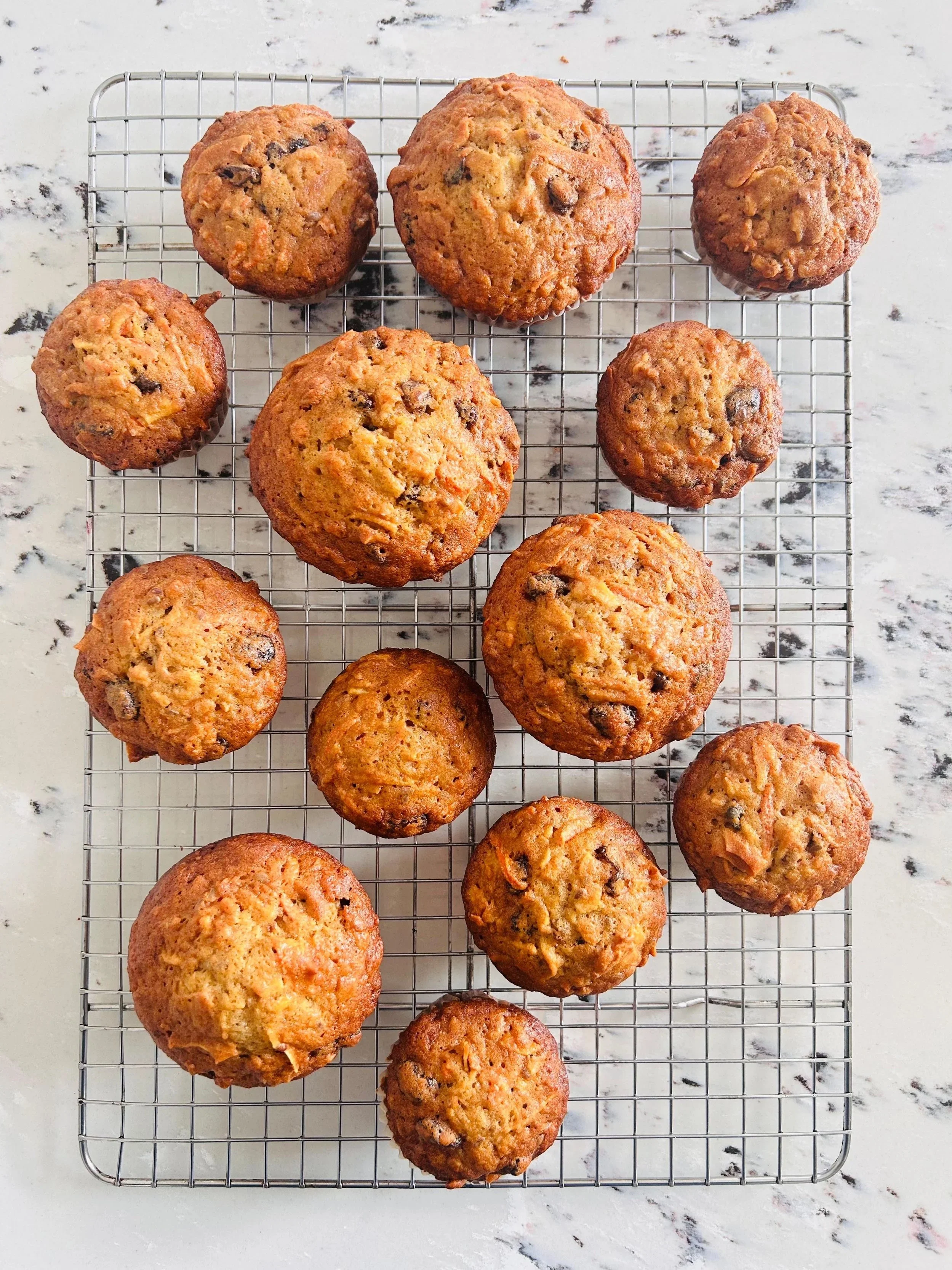 A group of chocolate chip muffins on a wire cooling rack placed on a marble countertop.